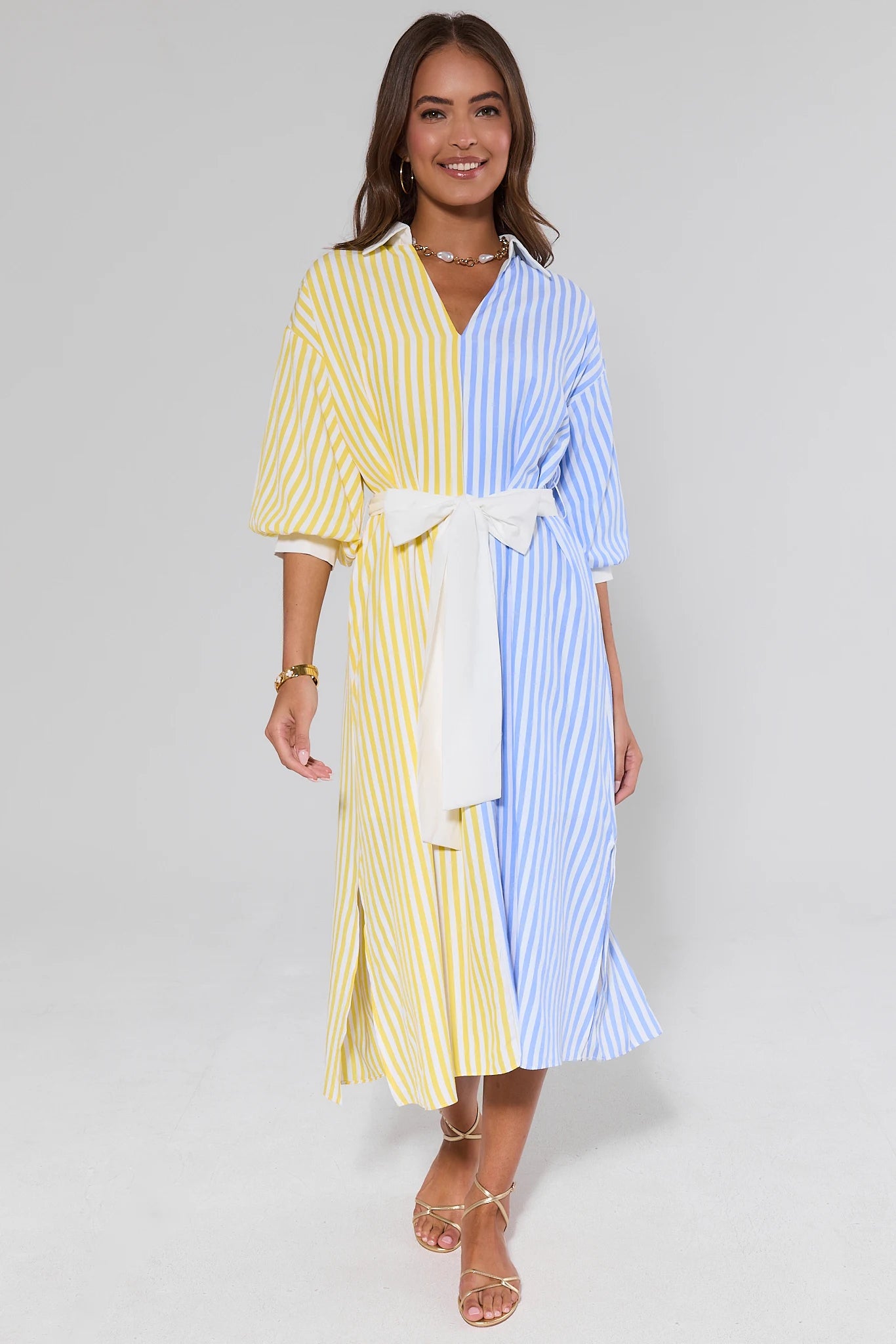 Woman wearing a two-tone striped dress and gold shoes with a white background