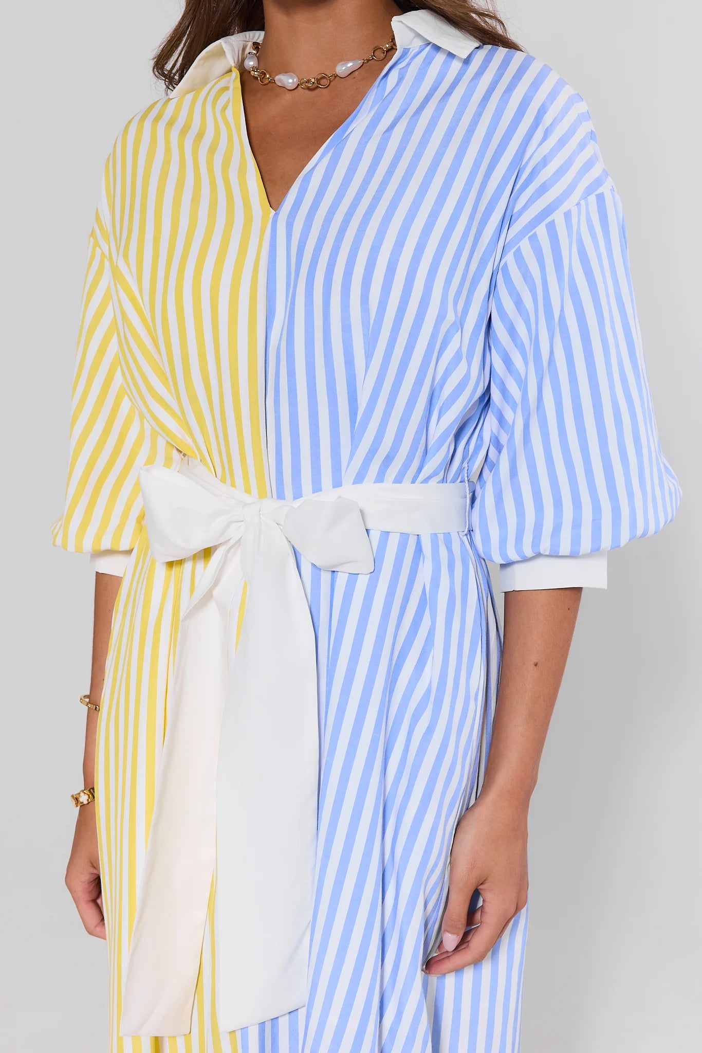 close up Woman wearing a blue and yellow striped dress with a white belt on a plain background