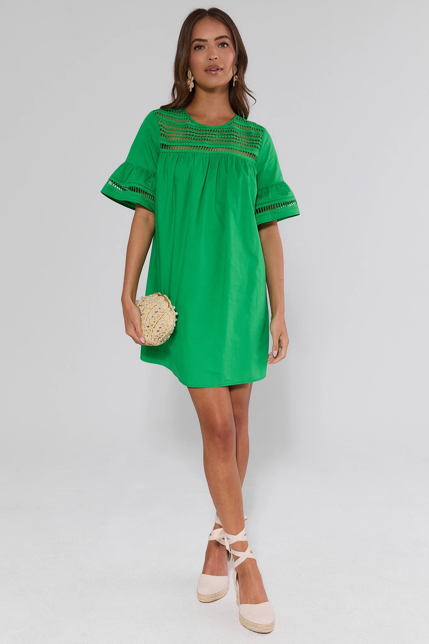 Woman wearing a green dress with embroidered details and earrings on a white background