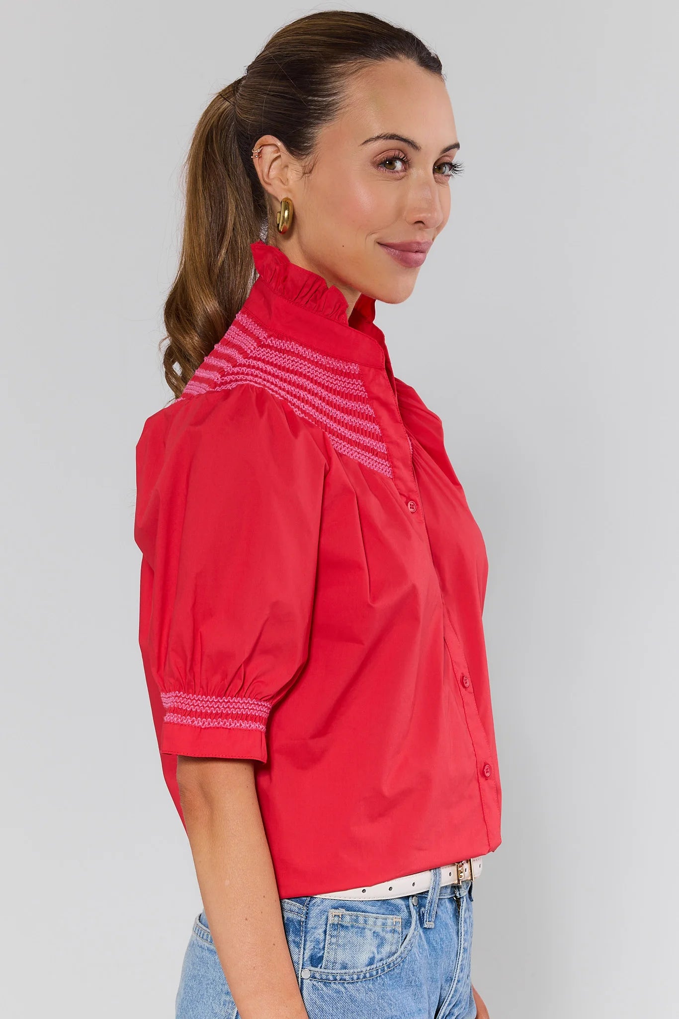 side shot Woman wearing a red jacket with white embroidery on a gray background