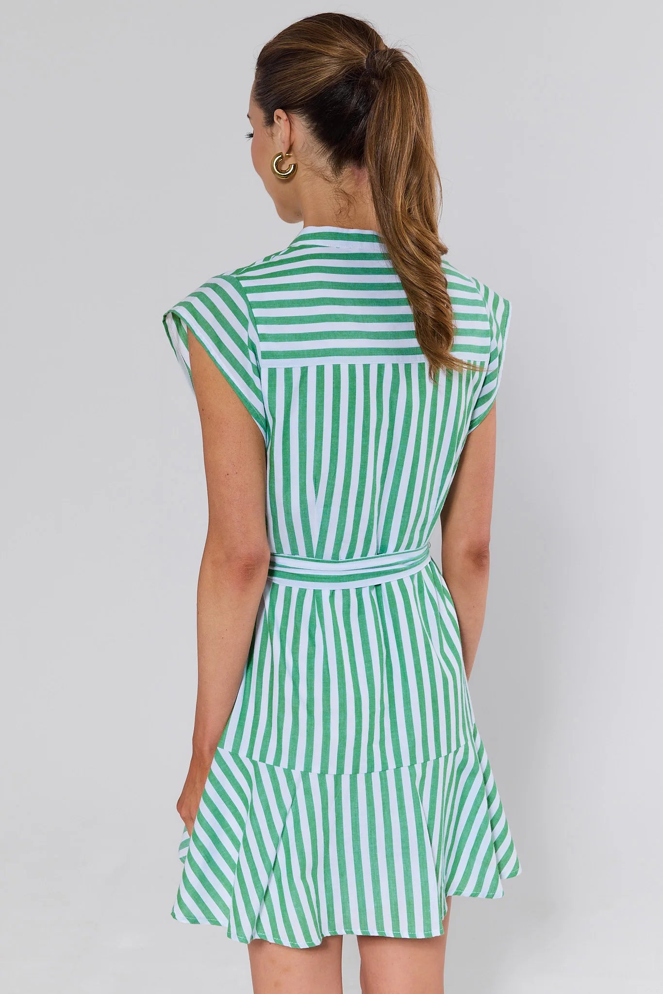 Woman standing wearing a green and white striped dress against a plain background