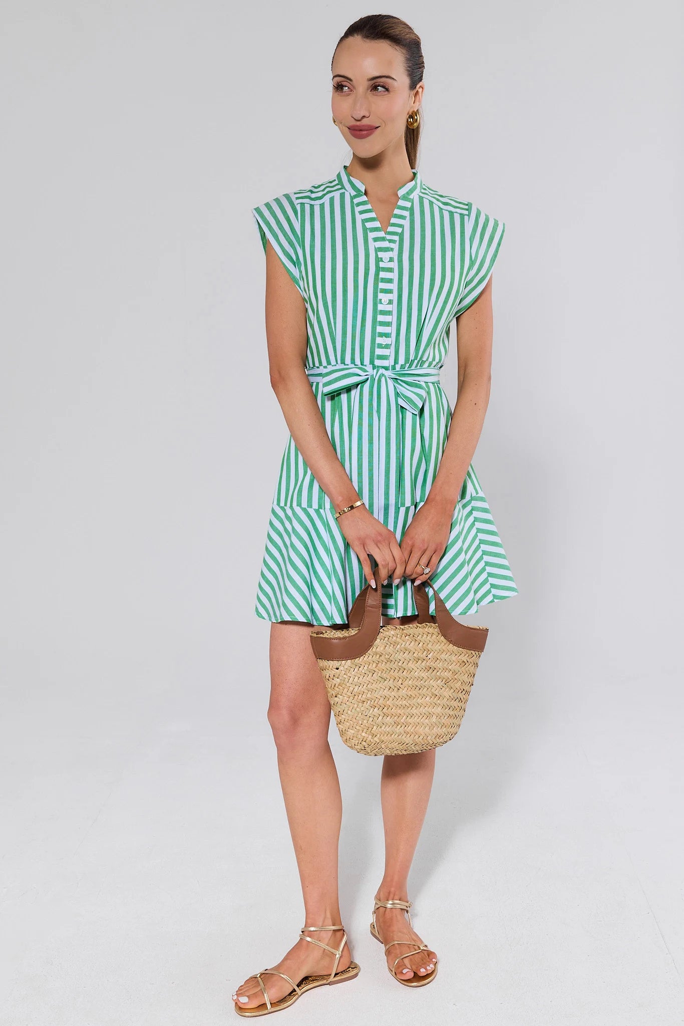 Woman wearing a green and white striped dress holding a straw bag on a white background