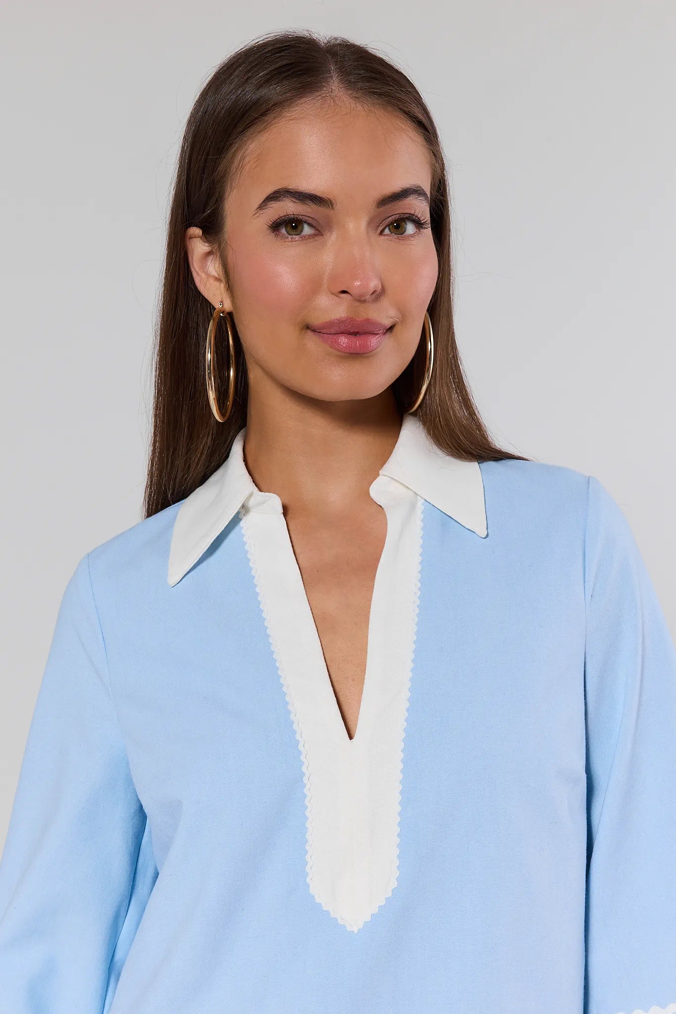 Woman wearing a light blue blouse with a white collar against a plain background