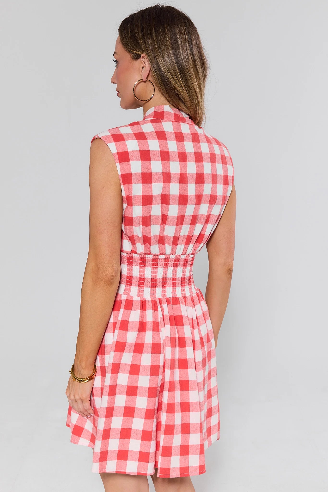 Woman standing wearing a red and white checkered dress against a plain background