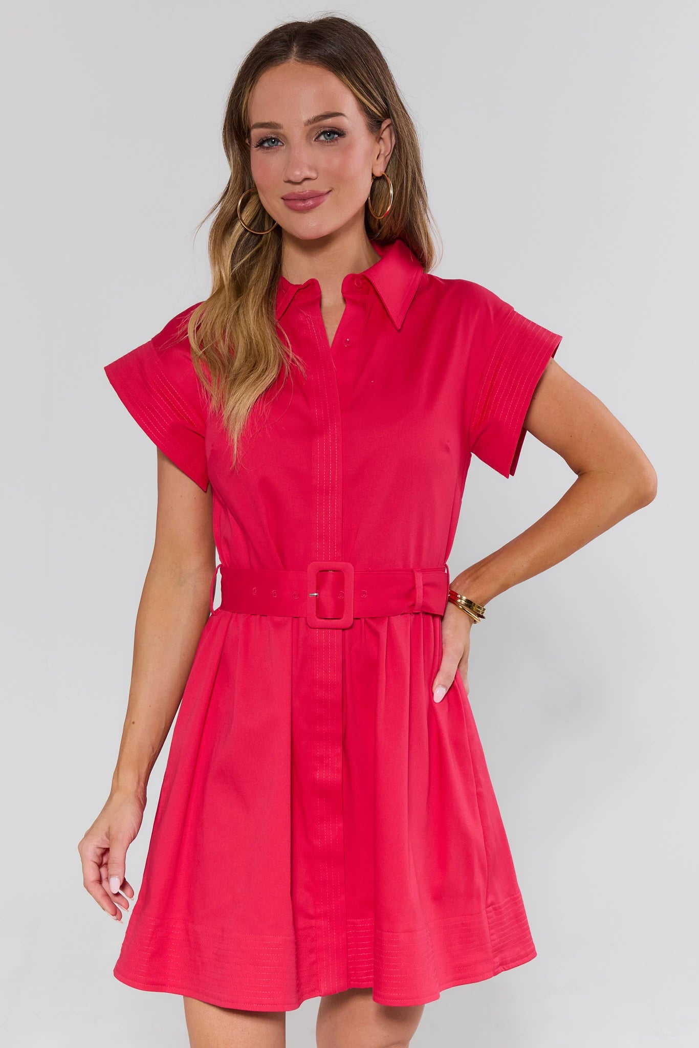 Woman wearing a bright pink dress with a belt against a white background