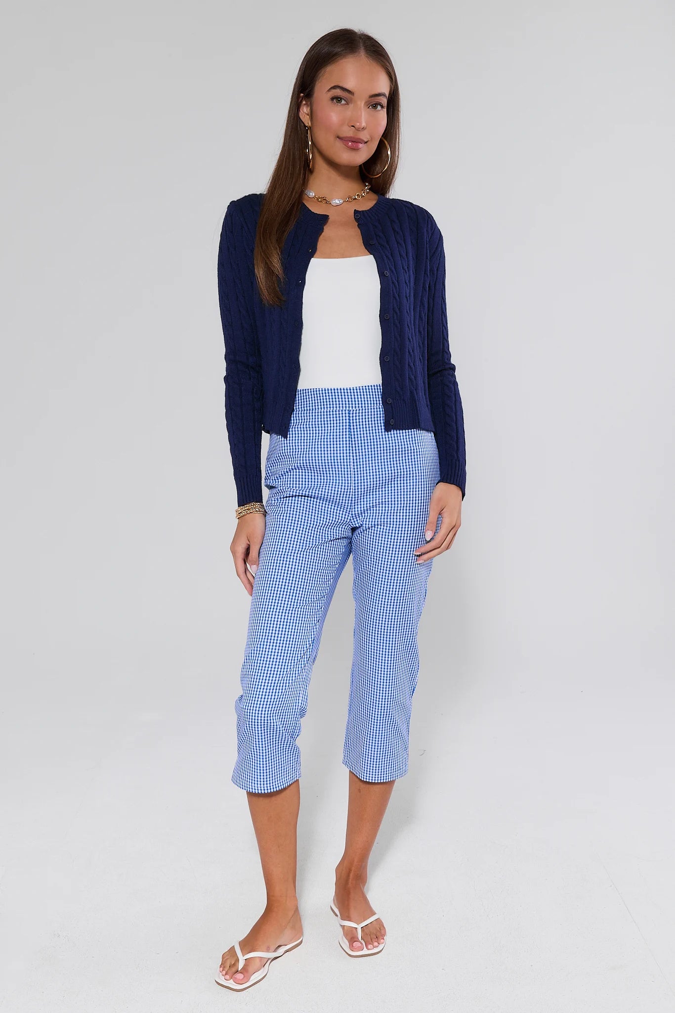 Woman wearing a navy cardigan, white top, and blue checkered pants on a white background