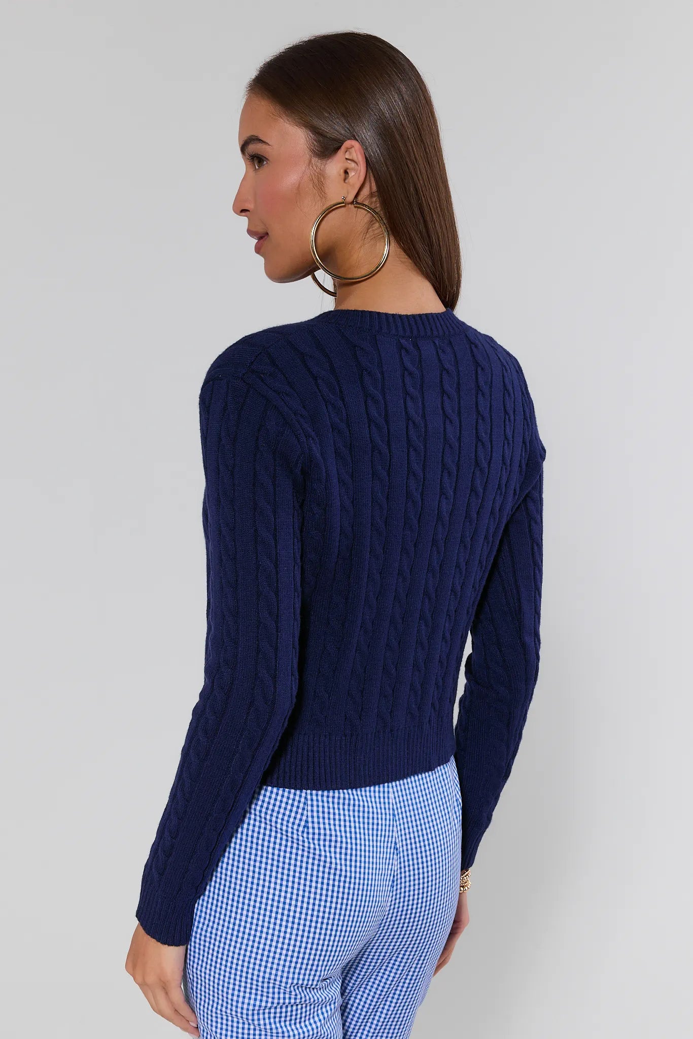 Woman wearing a navy blue cable knit sweater and blue checkered pants against a plain background