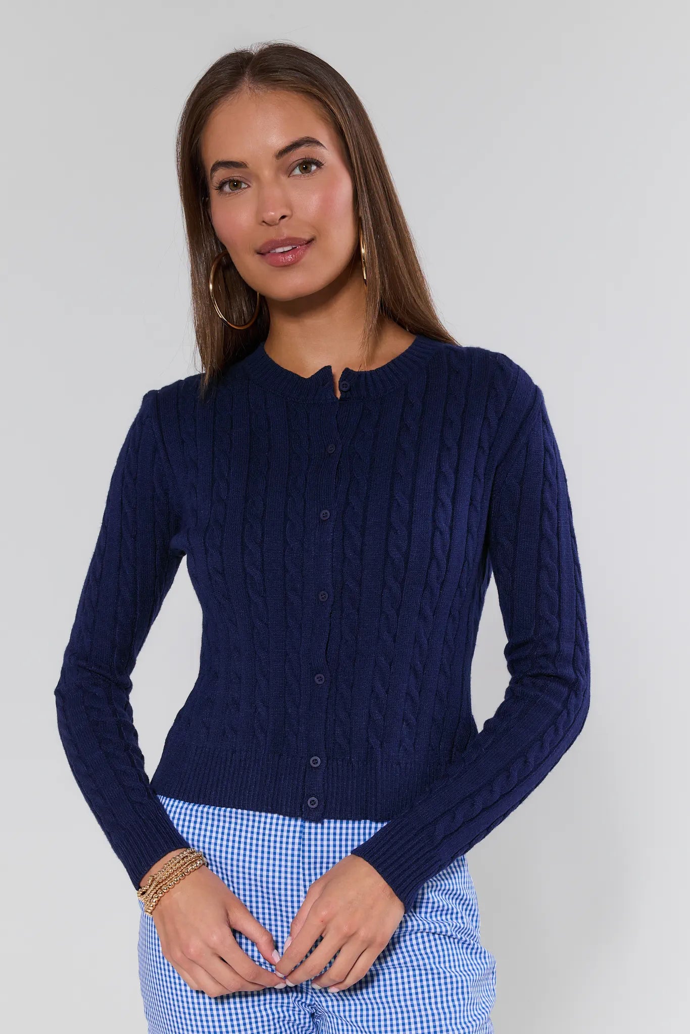 Woman wearing a navy blue cable knit cardigan over a blue checkered dress on a white background