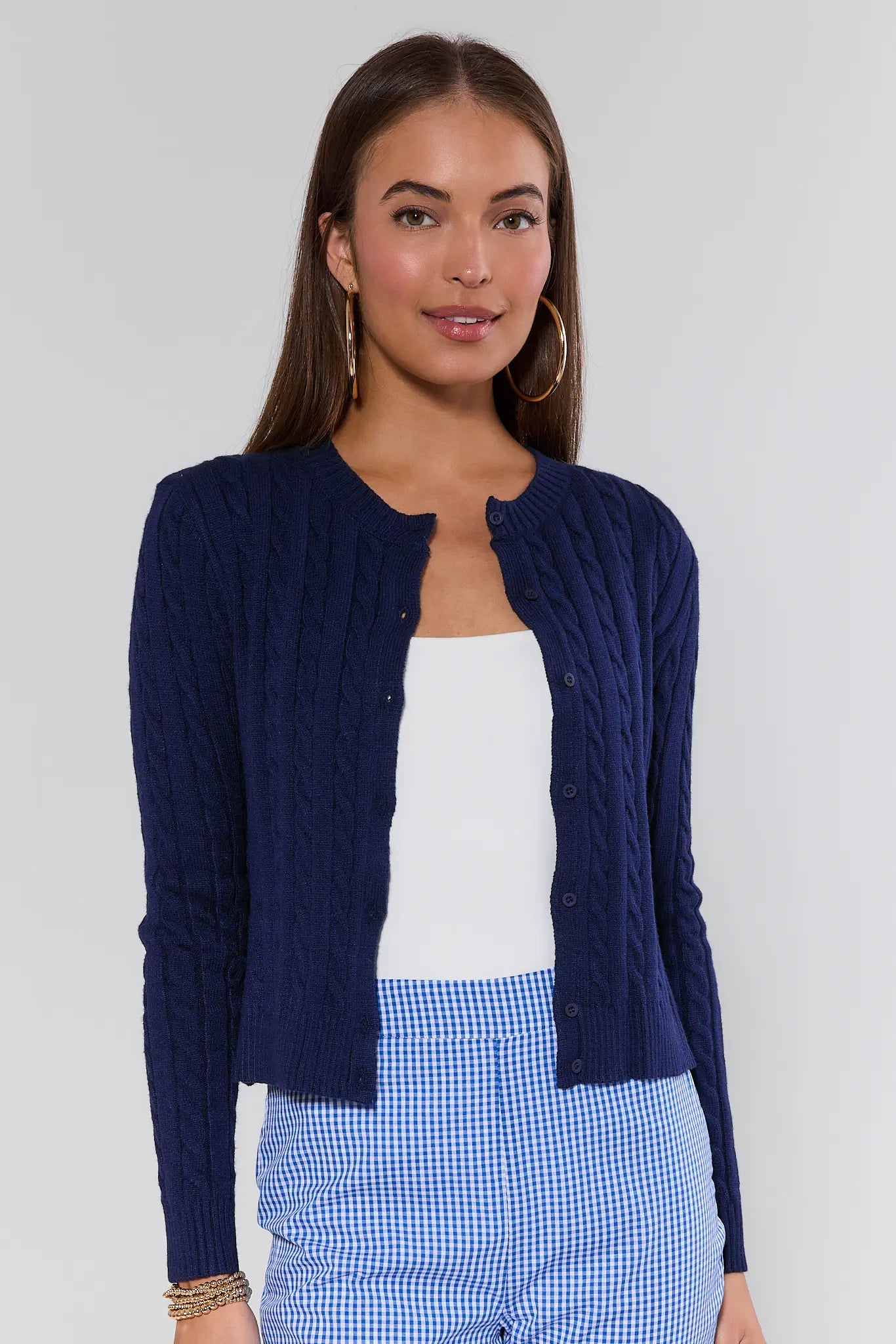 Woman wearing a navy blue cardigan over a white top and blue checkered pants on a plain background