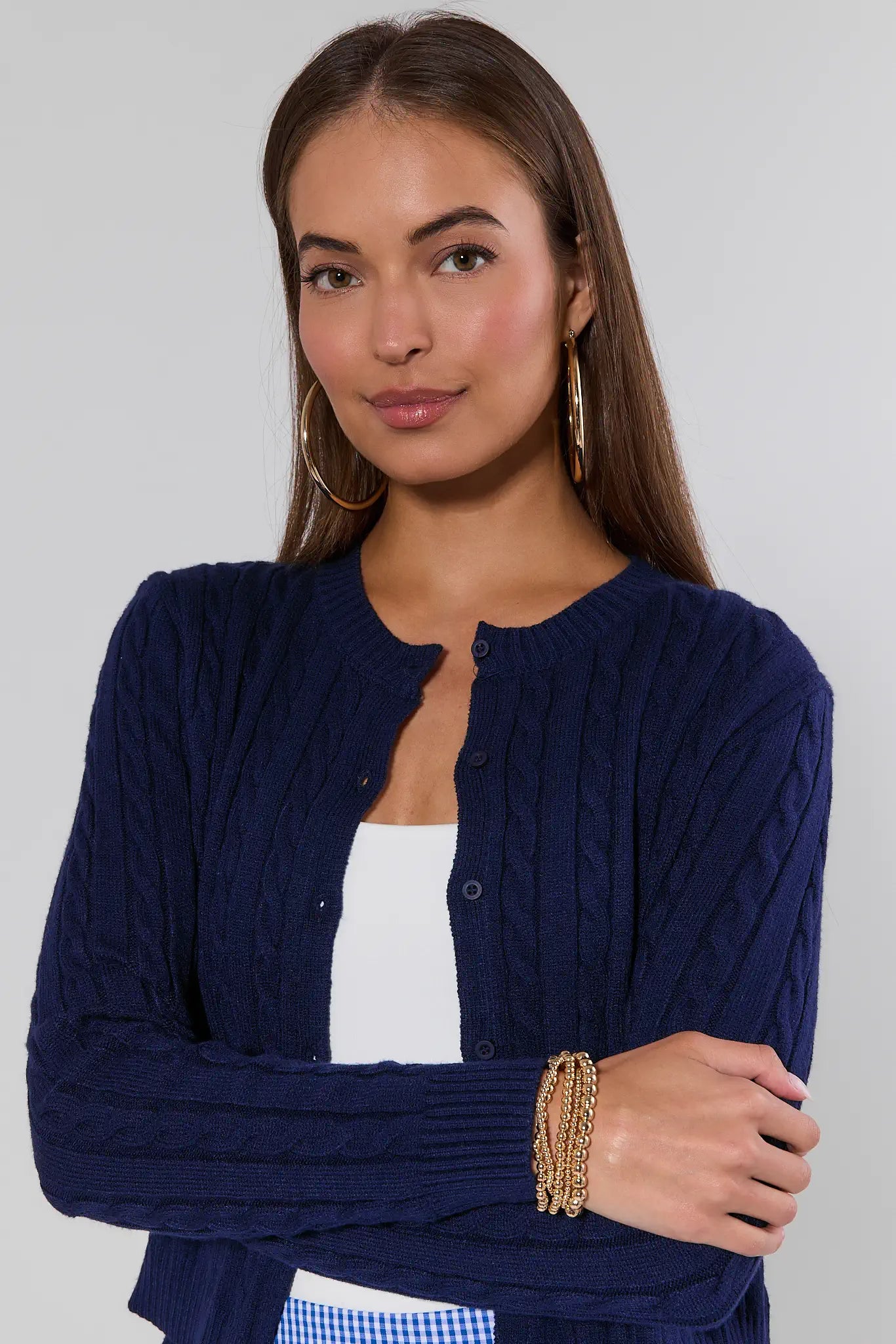 Woman wearing a navy blue cardigan over a white top with a gold bracelet on a plain background