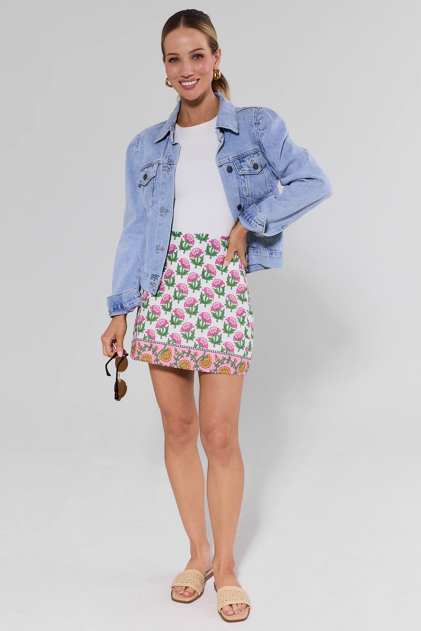 Woman wearing a denim jacket, white top, and cactus print skirt on a plain background