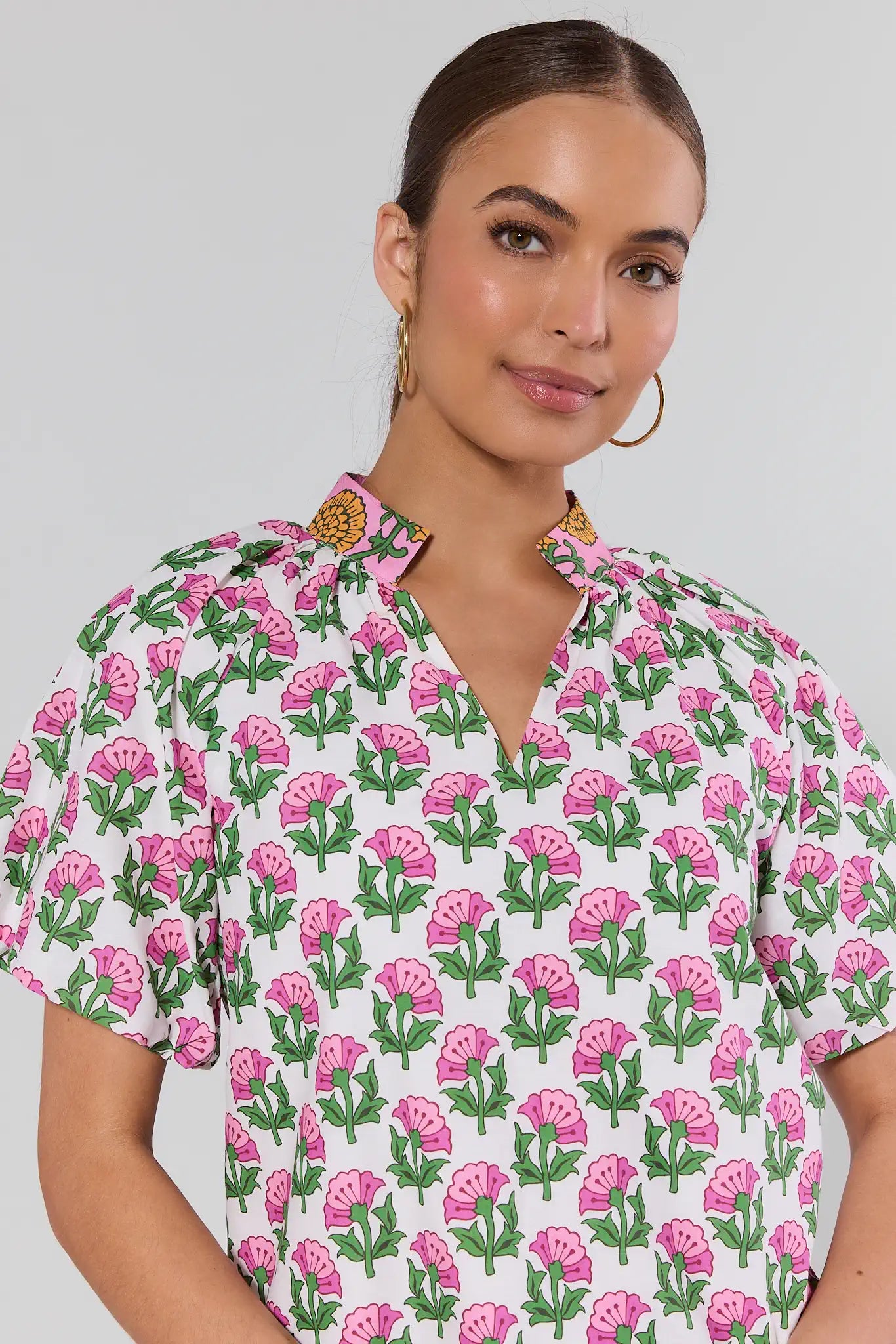 Woman wearing a floral patterned shirt with pink flowers and green leaves on a plain background