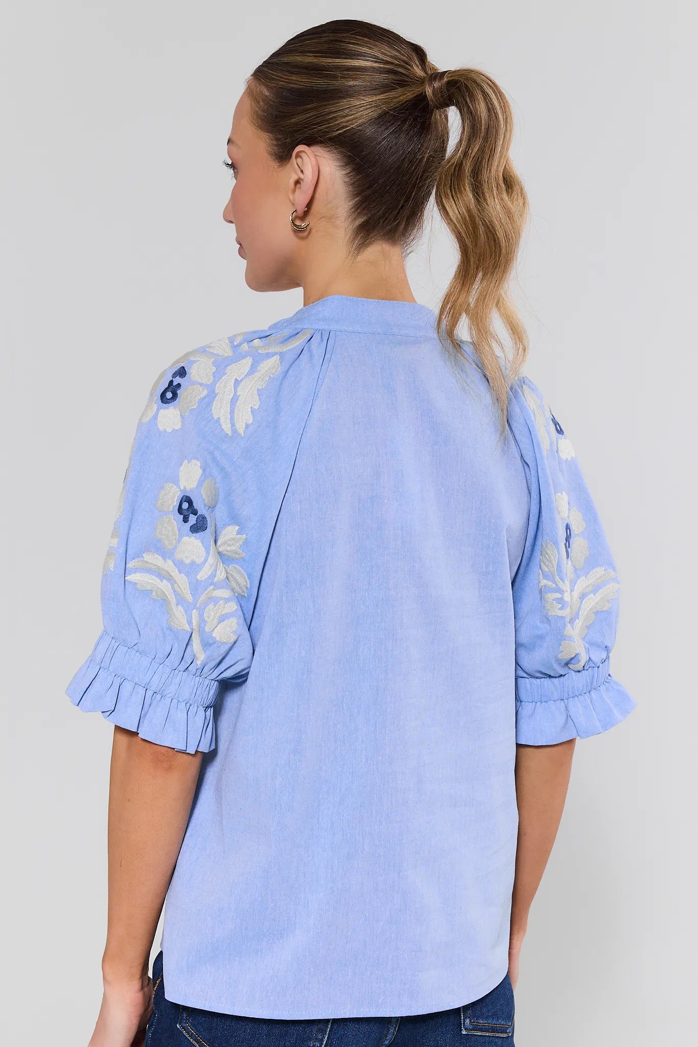 Woman wearing a light blue embroidered blouse against a background