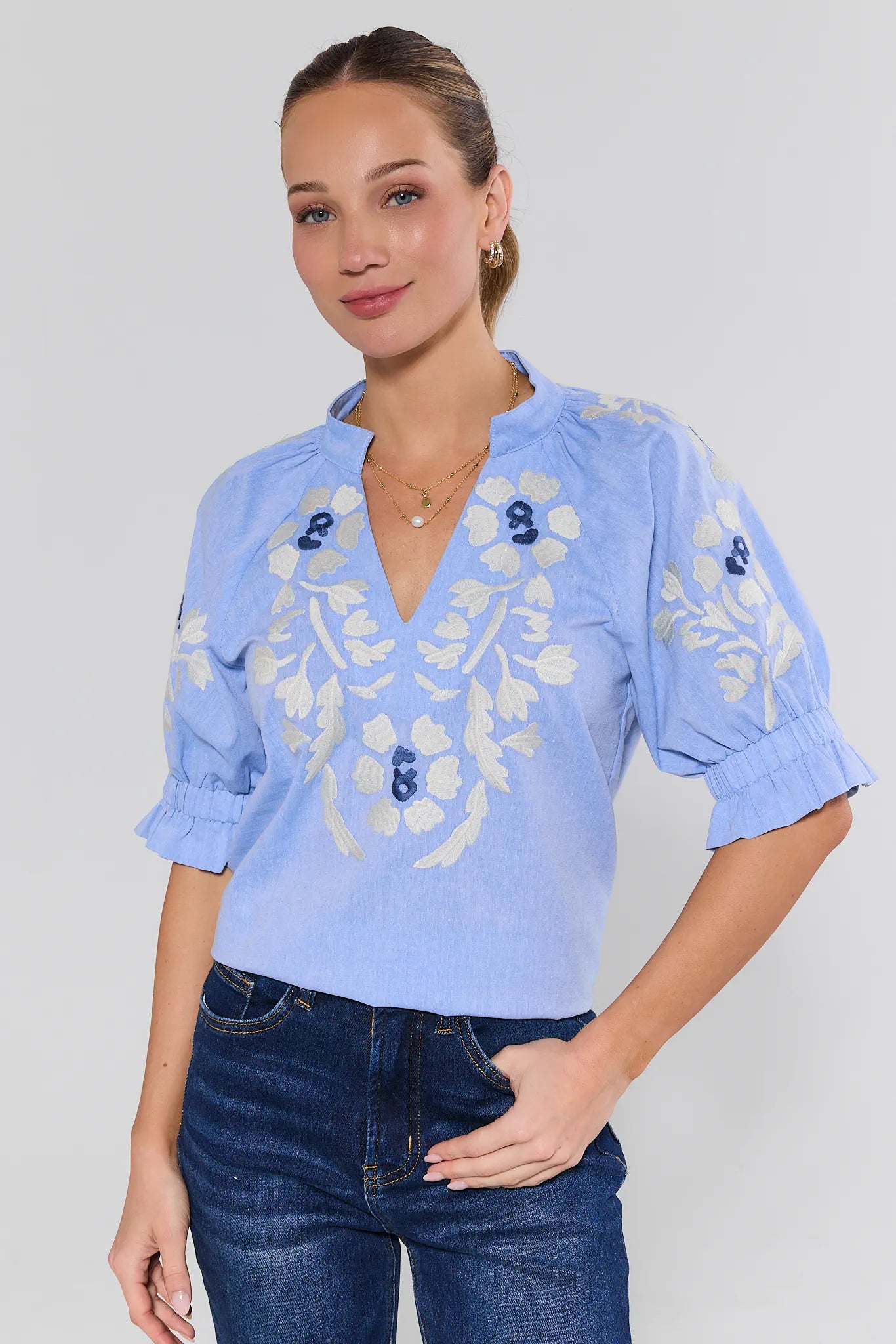 Woman wearing a light blue blouse with floral embroidery on a plain background
