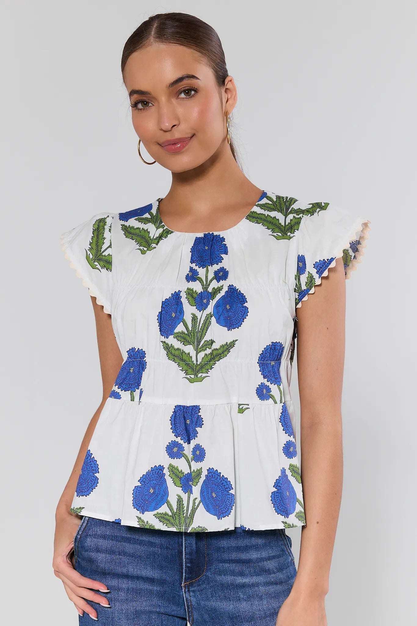 Woman wearing a white blouse with blue floral pattern on a plain background