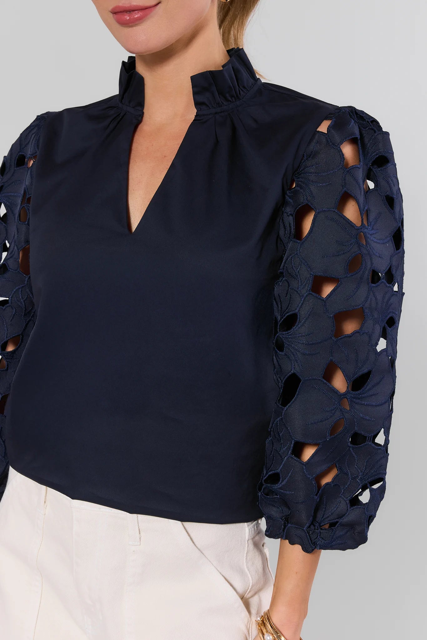 Navy Eyelet Sleeve Top by THML with ruffled collar, V-slit, and floral lace three-quarter sleeves, paired with light-colored pants for a feminine look.