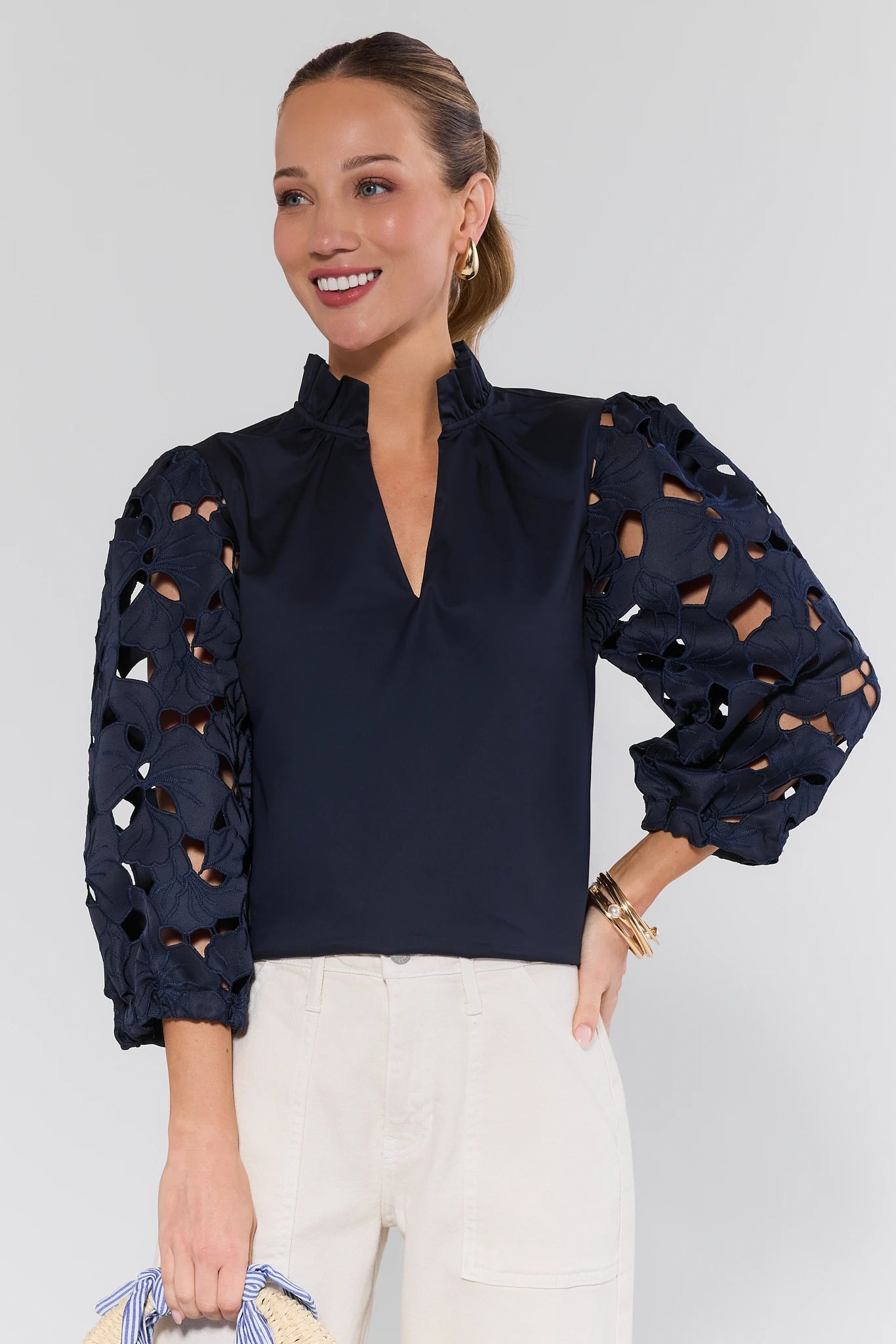 Model wearing the Navy Eyelet Sleeve Top by THML, featuring floral lace three-quarter sleeves, a ruffled collar, and a relaxed fit, paired with cream high-waisted pants.
