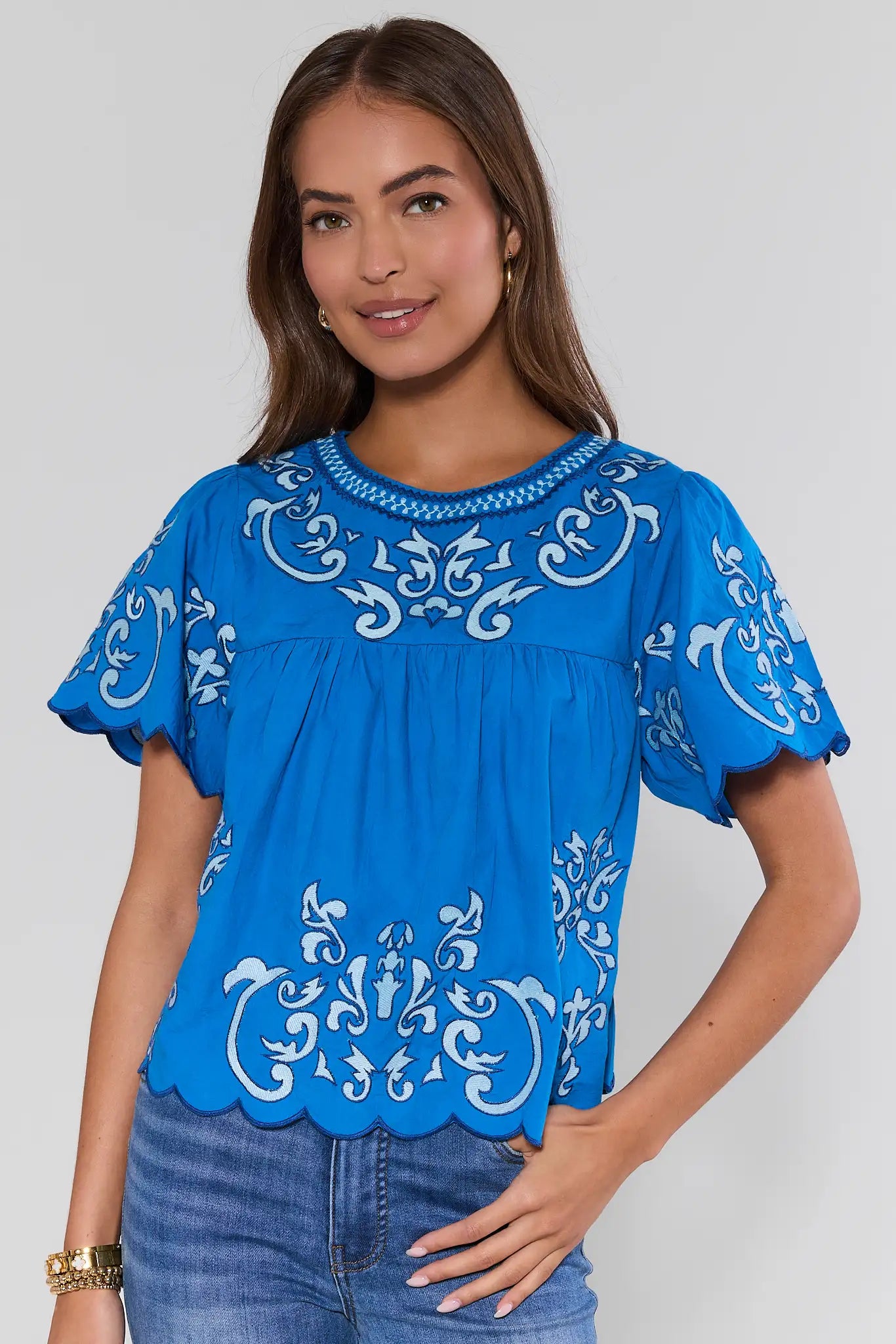 Woman wearing a blue embroidered top against a plain background