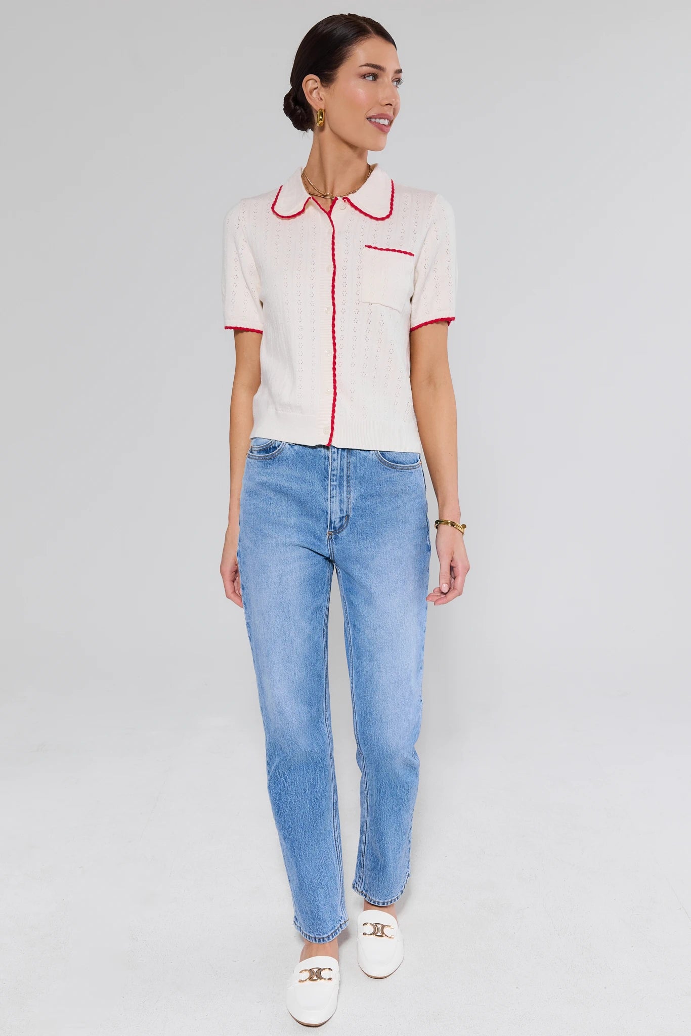 Woman wearing a white blouse with red accents and blue jeans on a light gray background