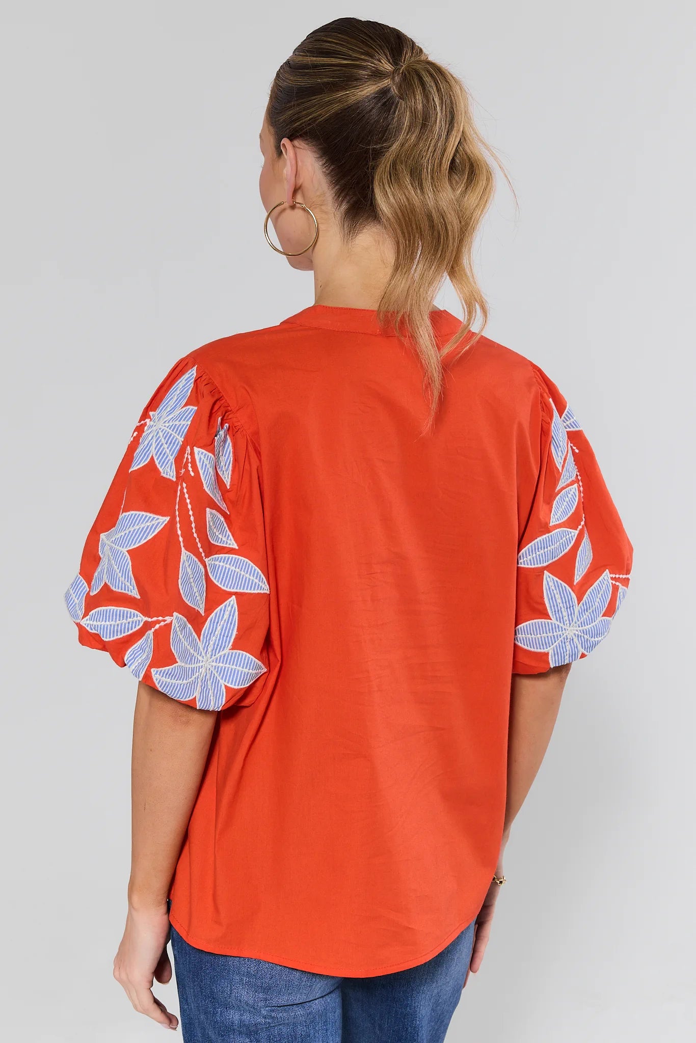 Woman wearing a red blouse with blue floral patterns on sleeves against a white background