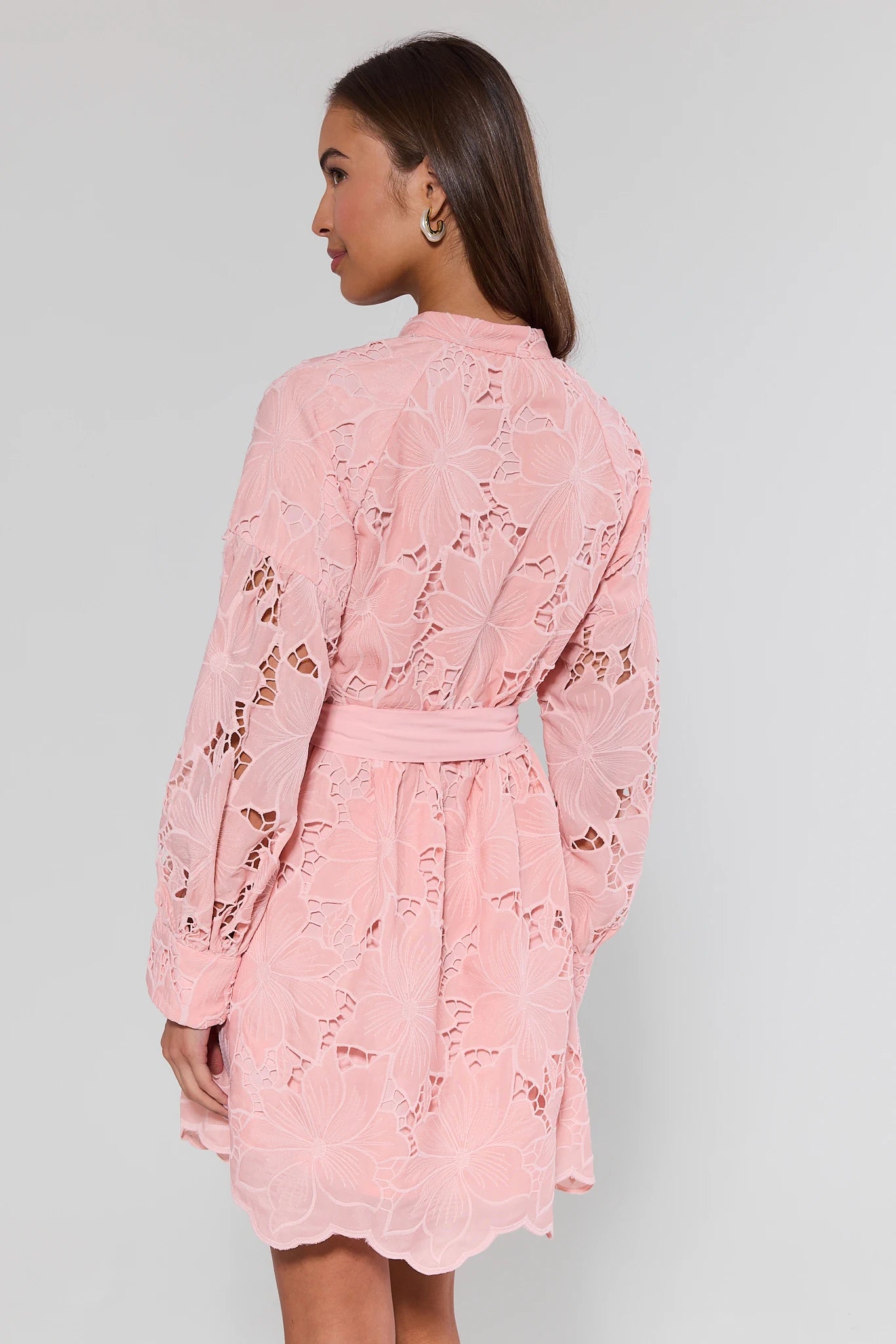 Woman wearing a pink lace dress against a gray background