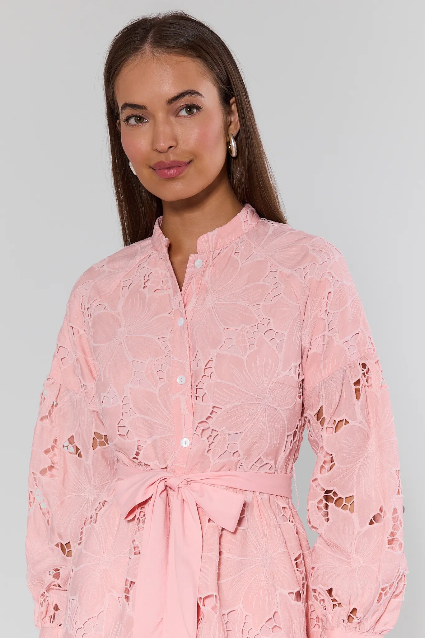 Woman wearing a pink lace dress against a plain background