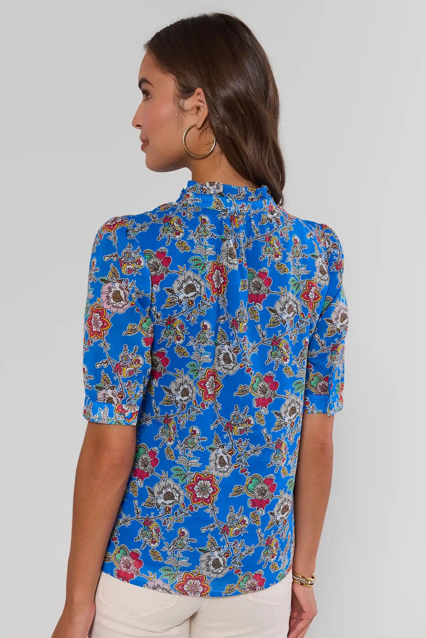 Woman wearing a blue floral blouse against a plain background standing