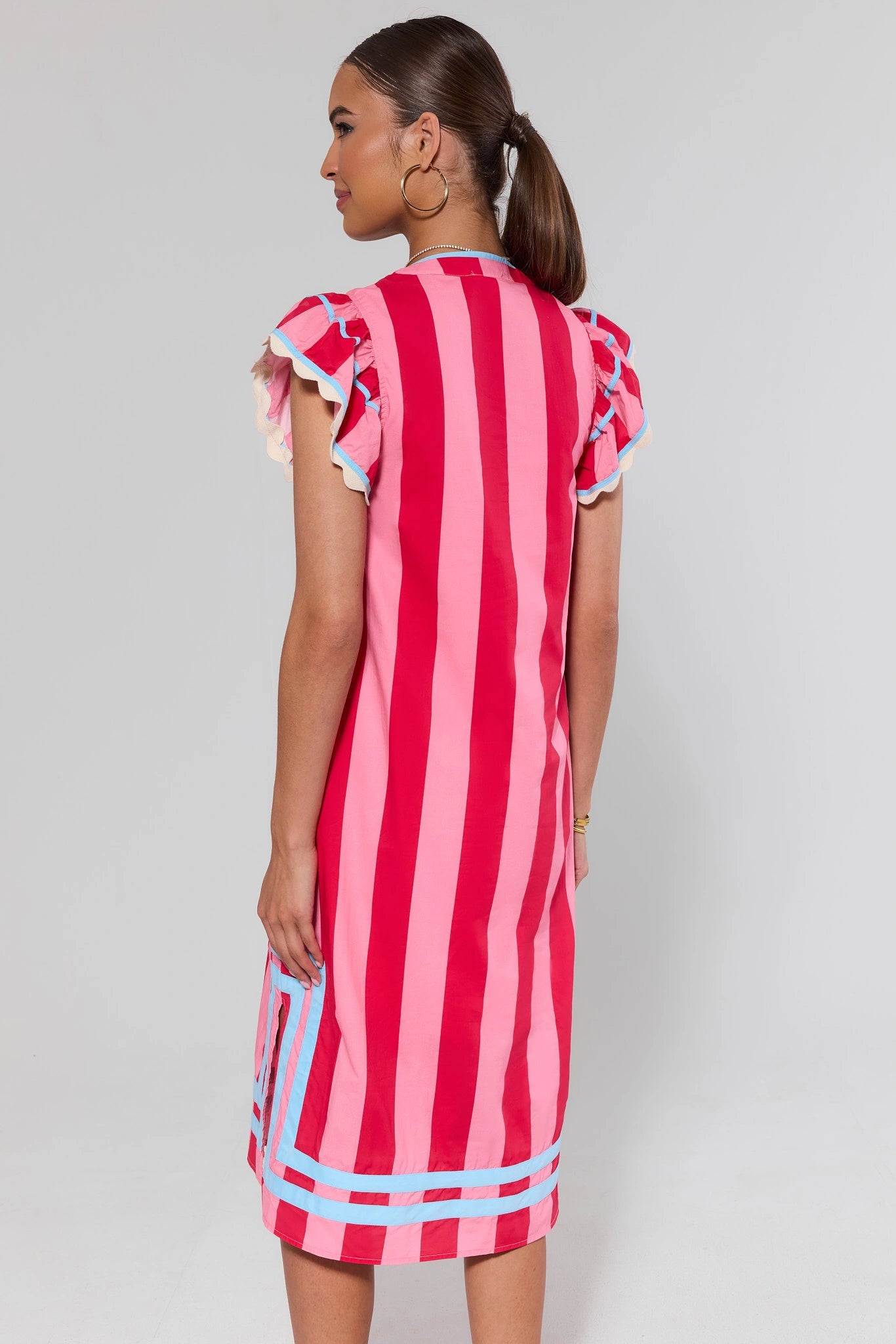 Woman standing wearing a red and pink striped dress with ruffled sleeves on a gray background
