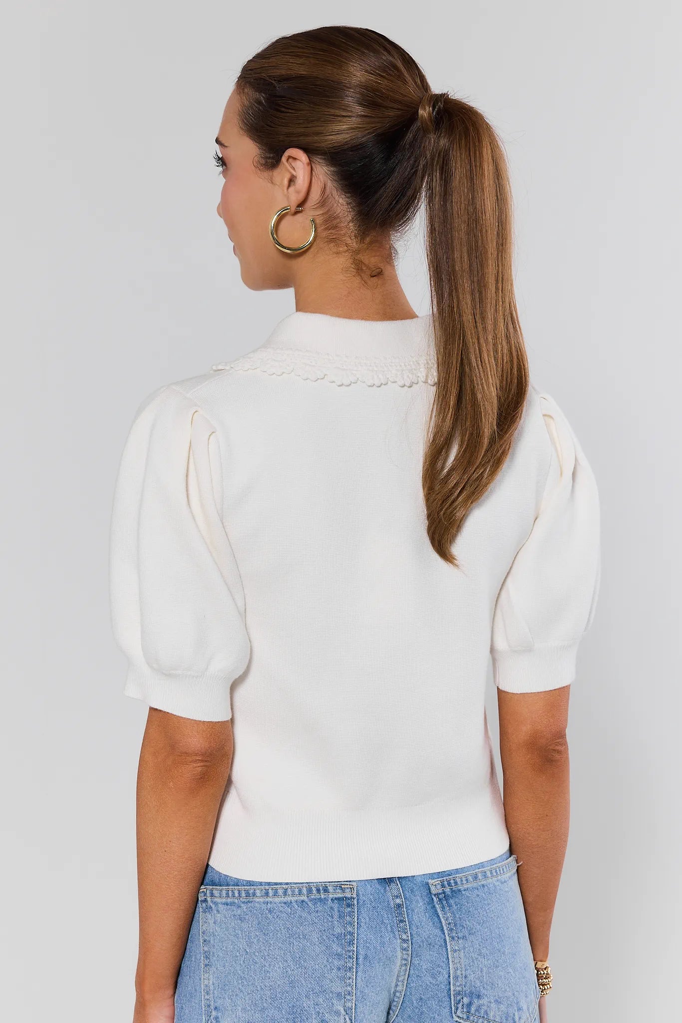 Woman wearing a white blouse and blue jeans against a plain background