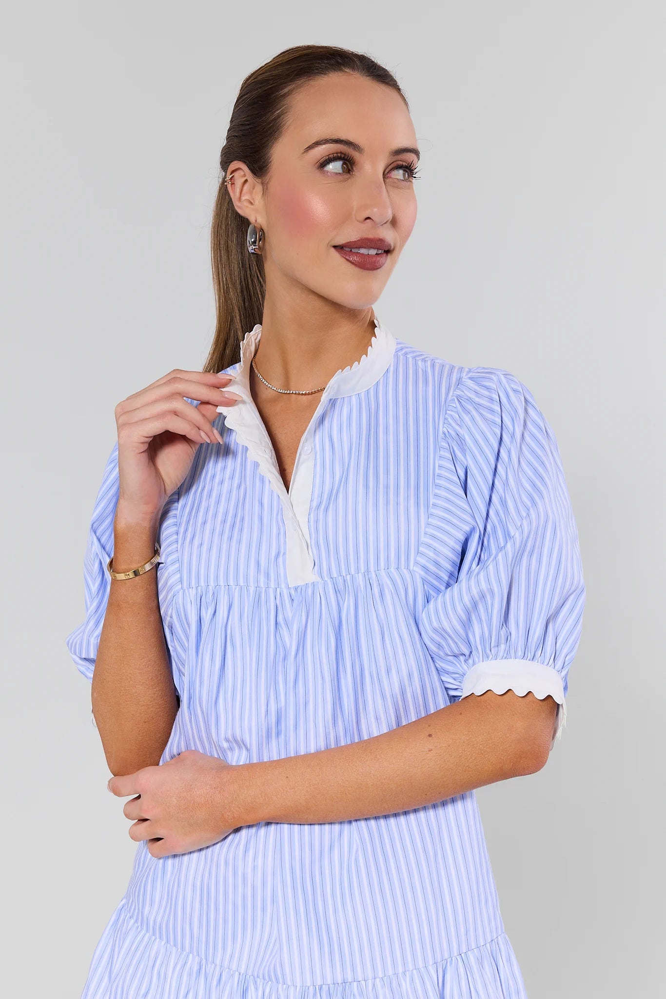 Woman wearing a light blue and white striped dress with a plain background