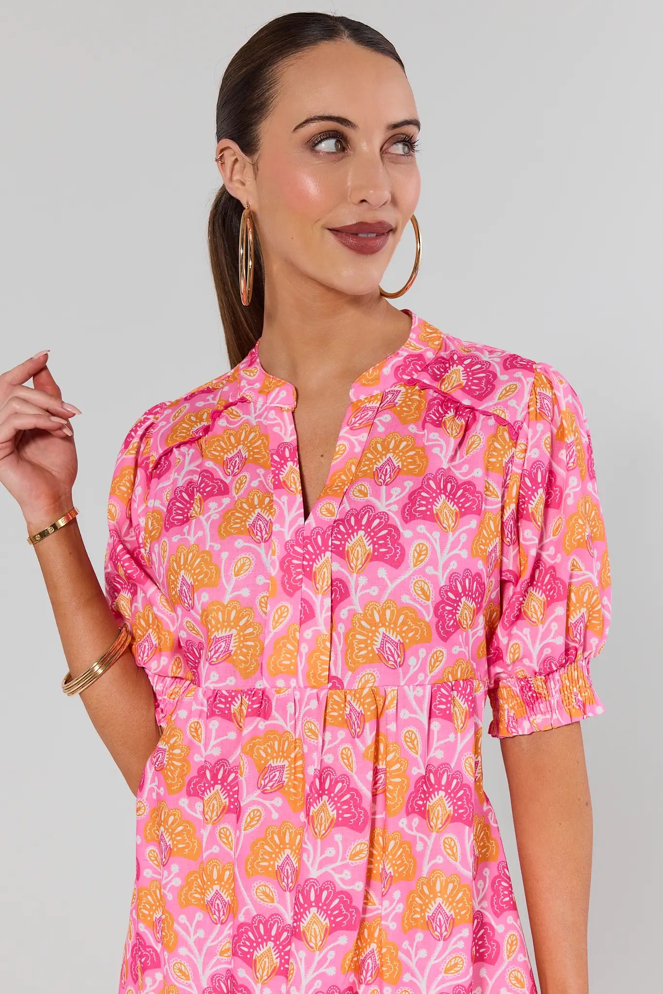 Woman wearing a pink and orange patterned dress against a gray background