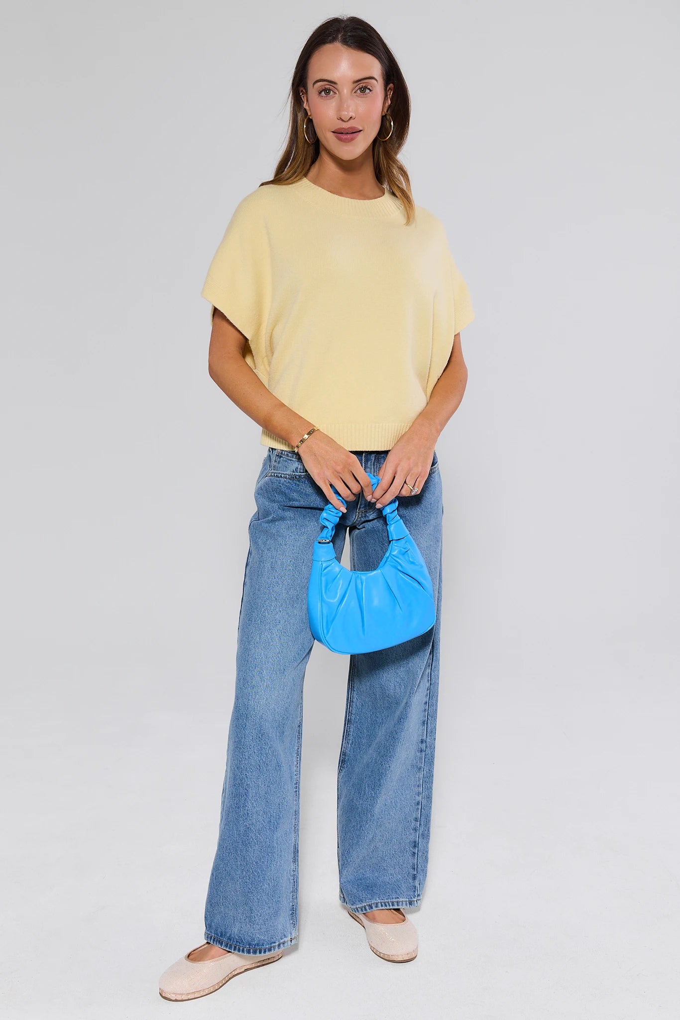 Woman holding a blue handbag wearing a yellow top and blue jeans on a white background