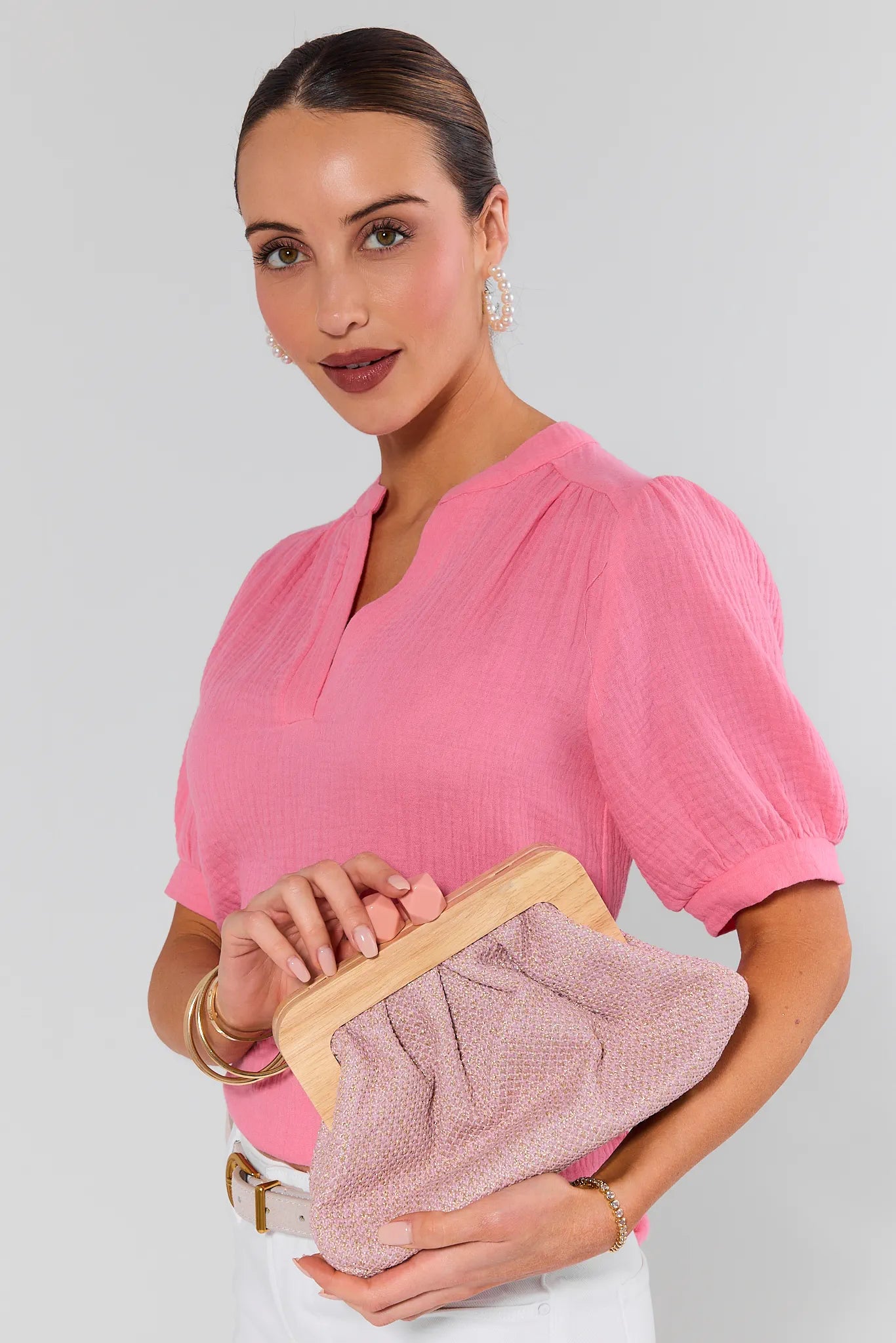 Woman in a pink blouse holding a pink clutch against a gray background