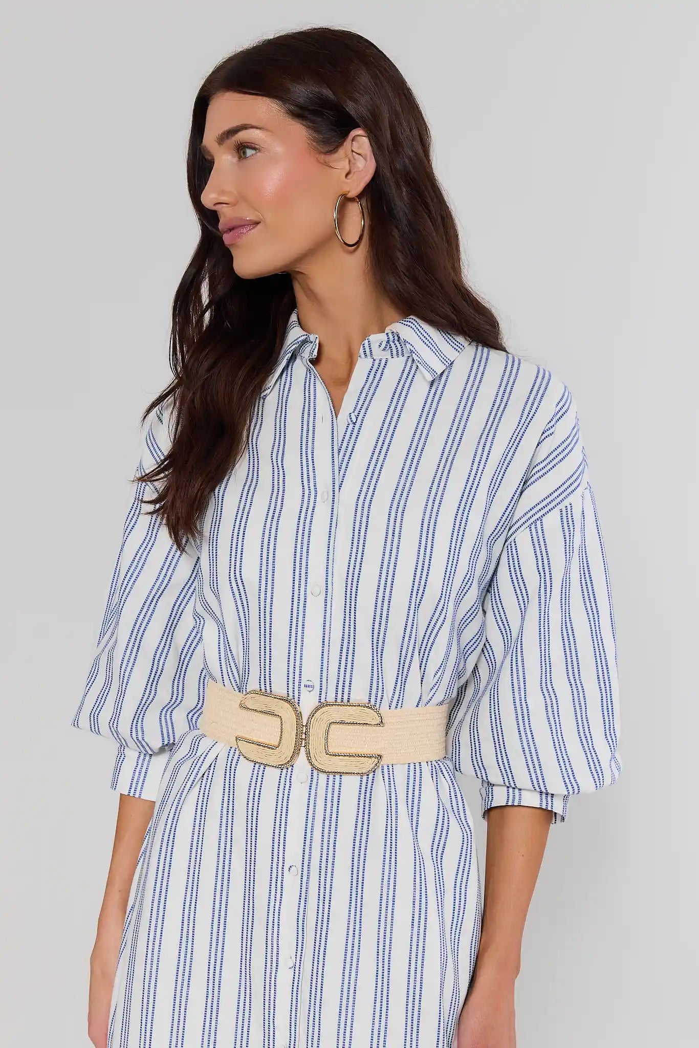 Woman wearing a blue and white striped dress with a beige belt on a plain background
