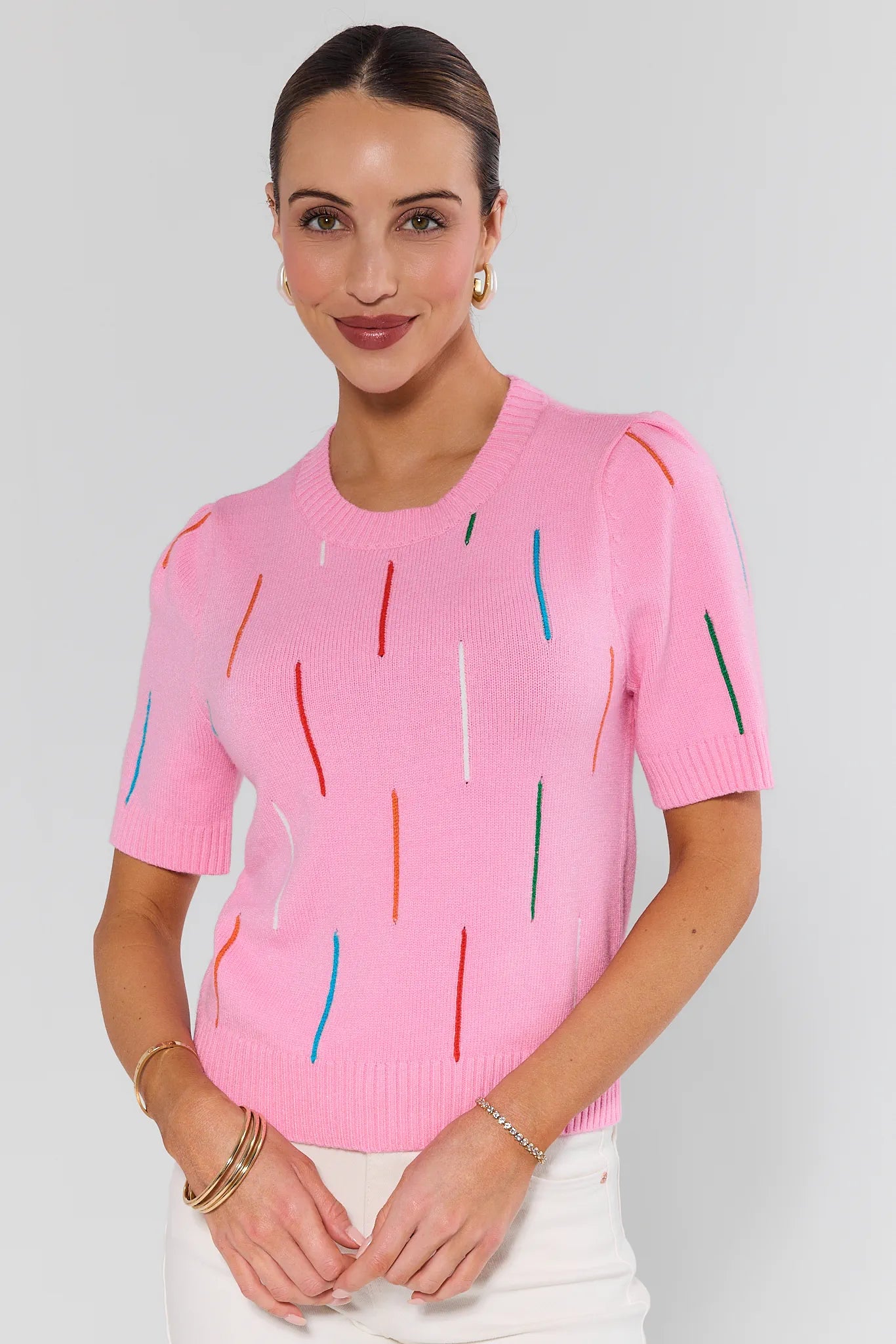 Woman wearing a pink sweater with colorful vertical stripes on a plain background