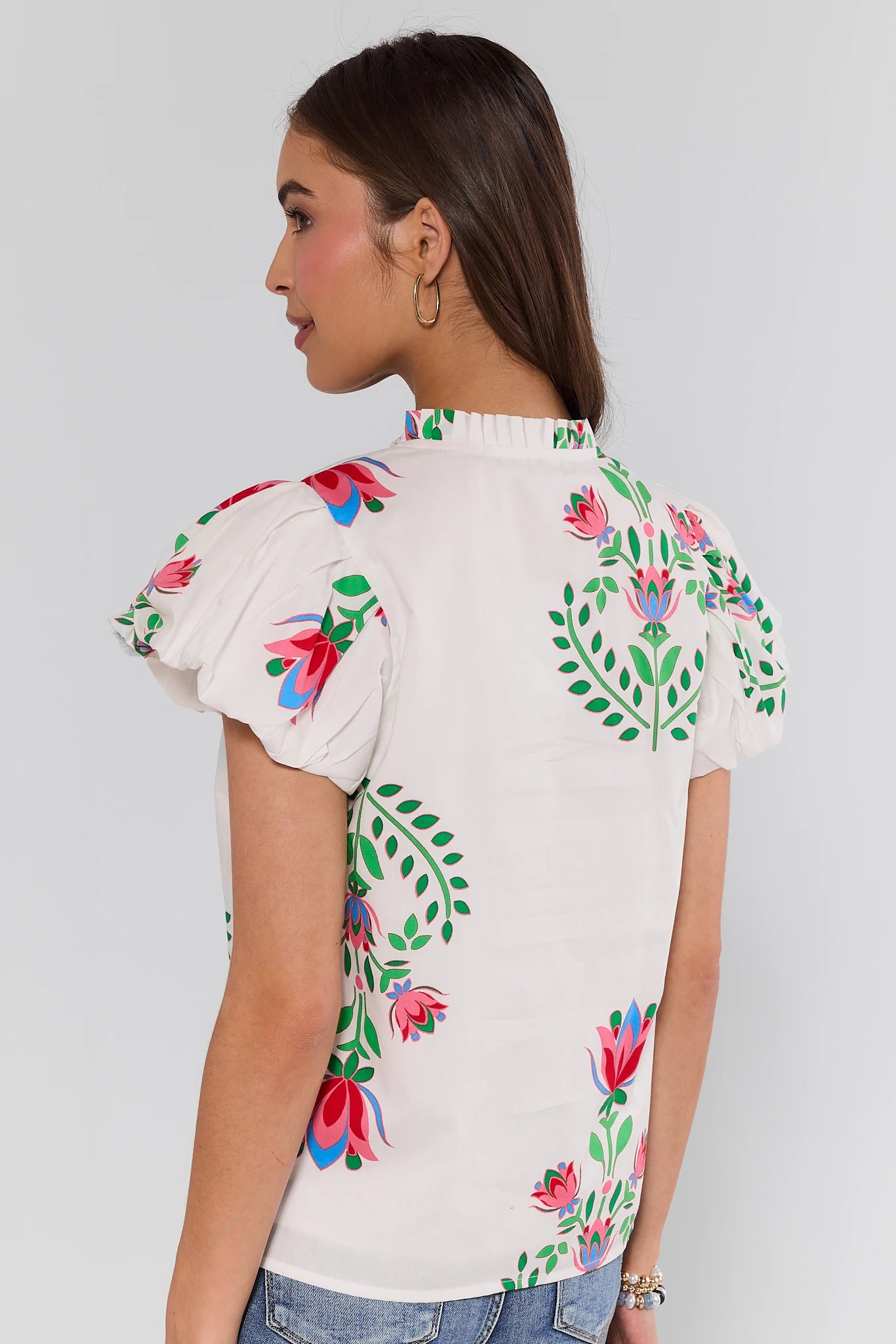Woman wearing a white blouse with colorful floral embroidery on a plain background