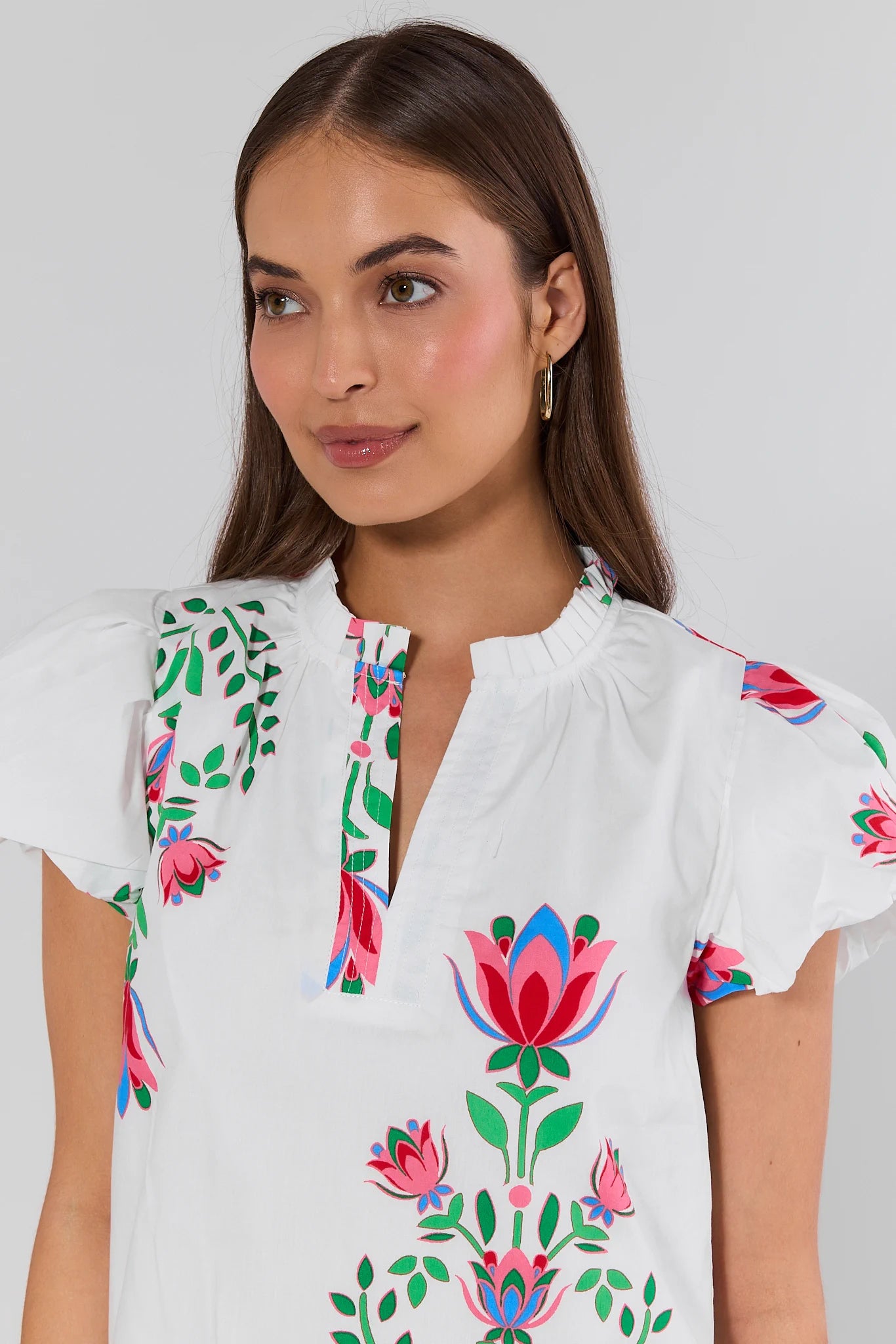 Woman wearing a white blouse with colorful floral embroidery on a plain background