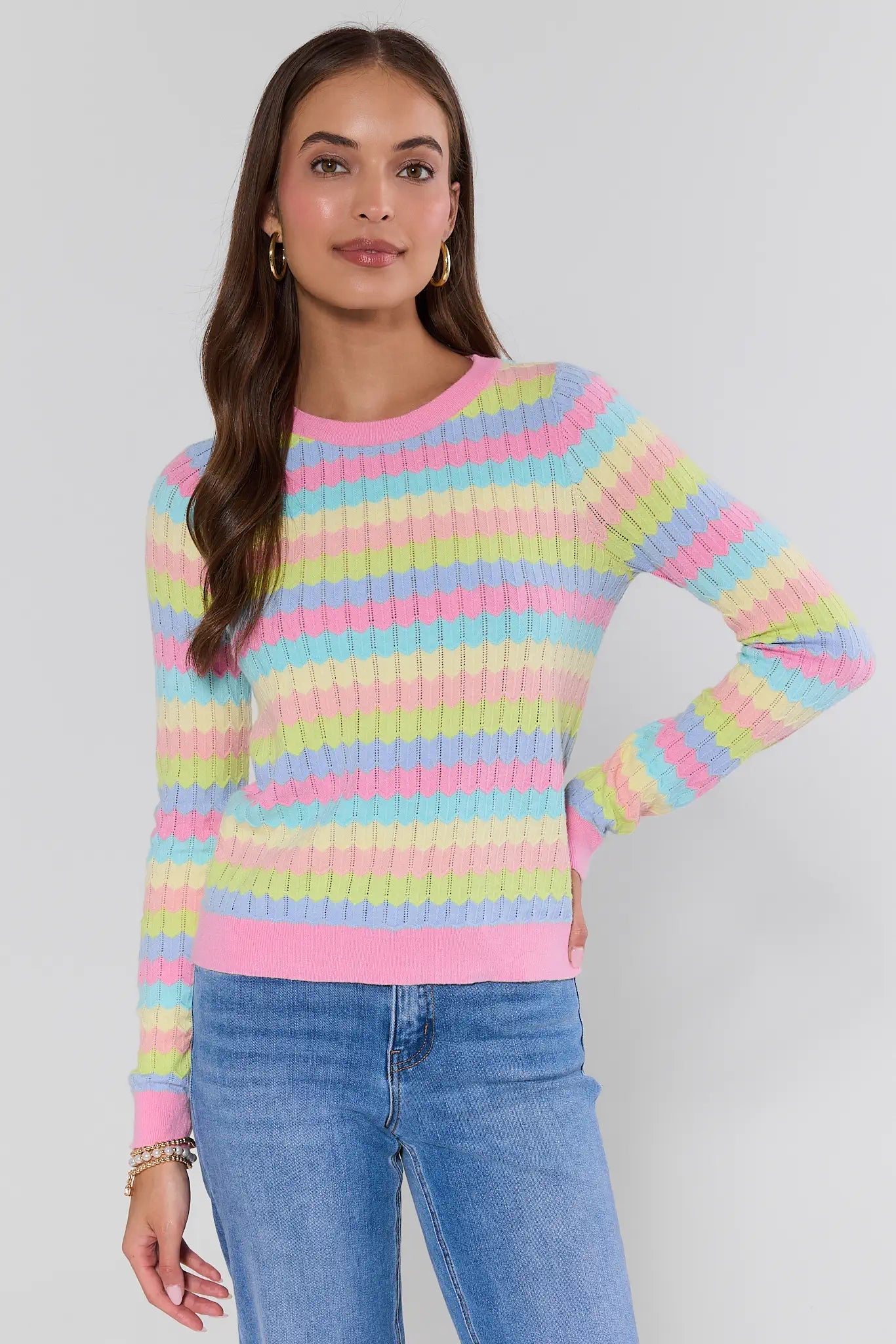 Woman wearing a colorful striped sweater and jeans against a plain background