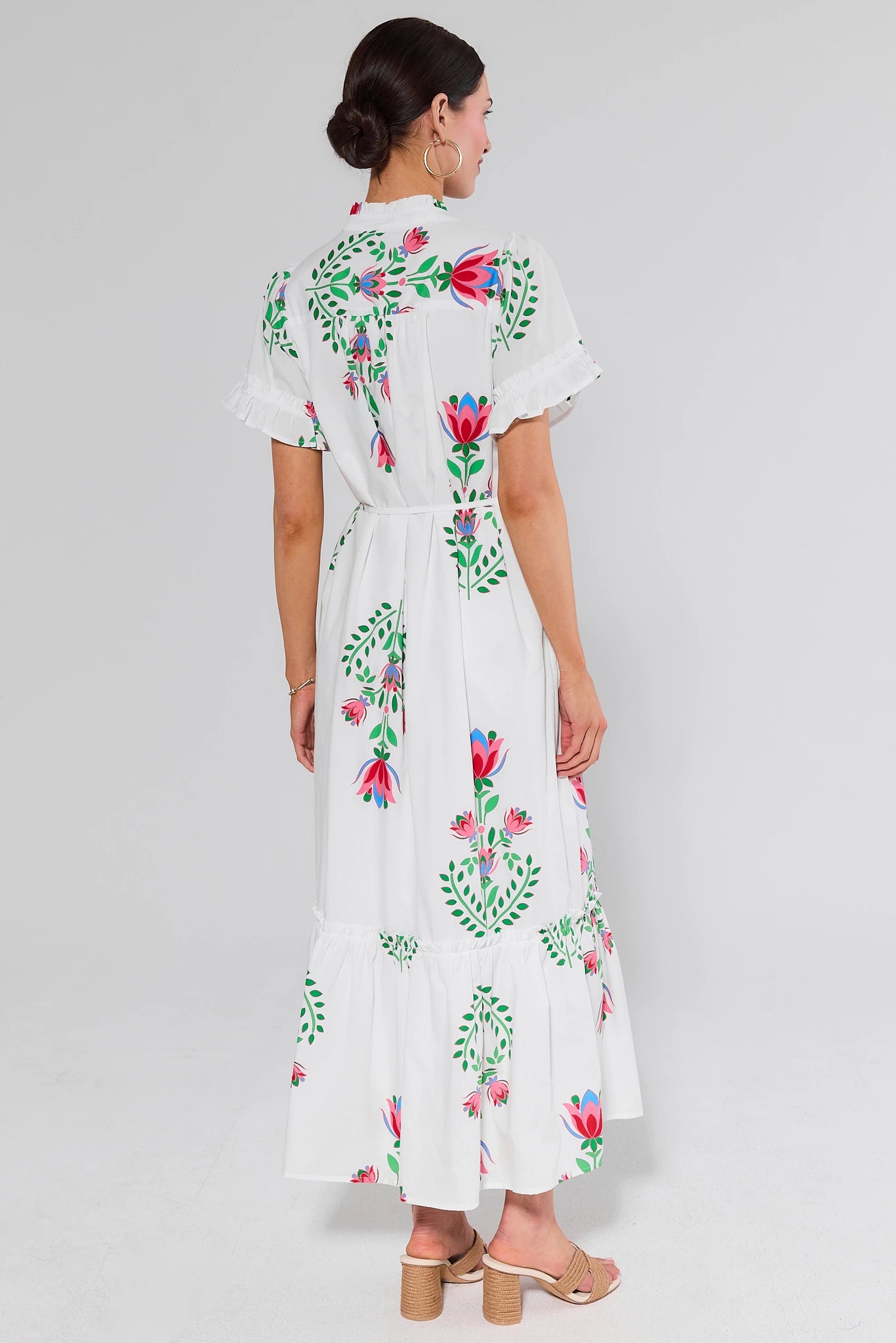 Woman standing wearing a white dress with colorful floral patterns on a plain background
