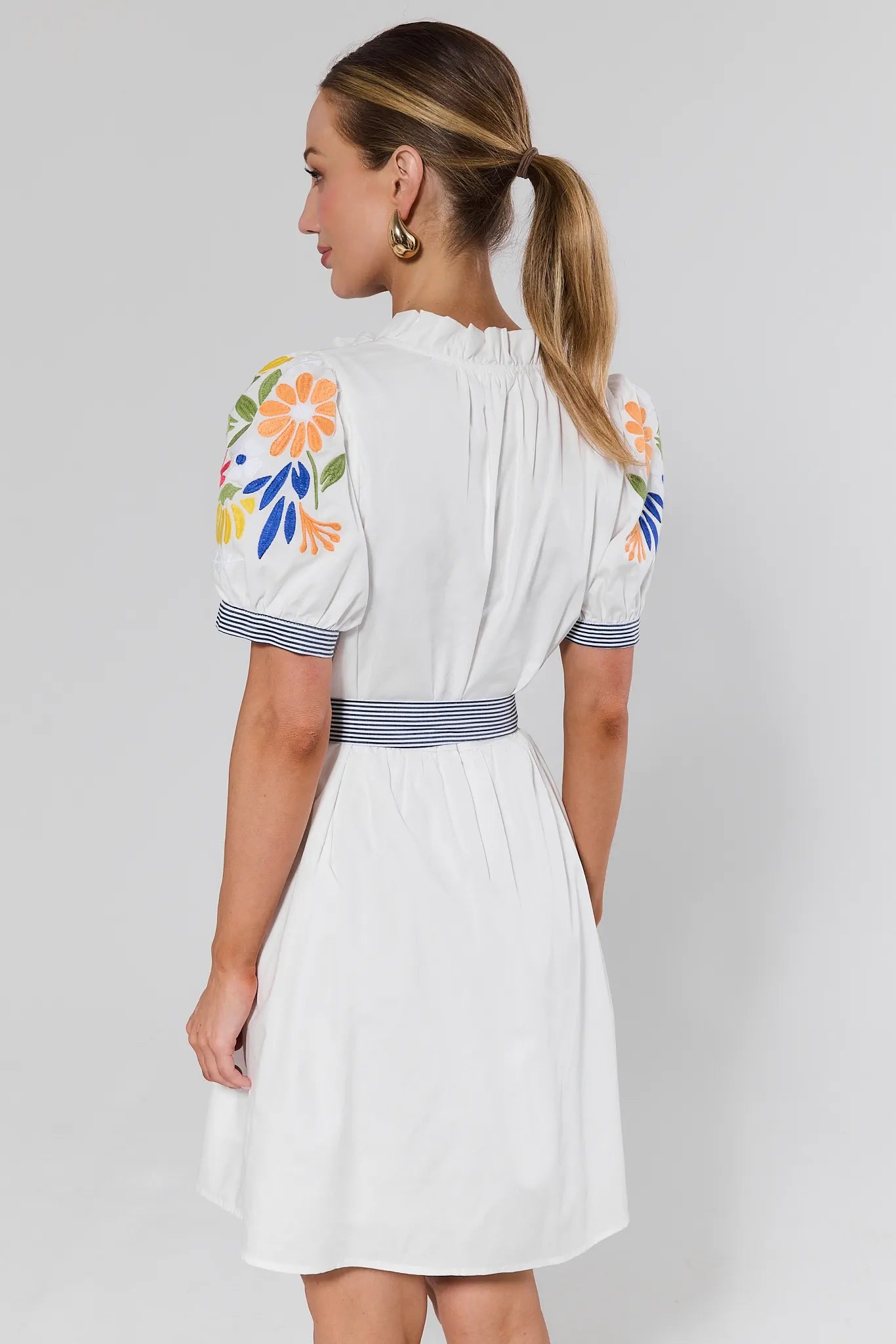 Woman wearing a white dress with floral embroidery on a plain background