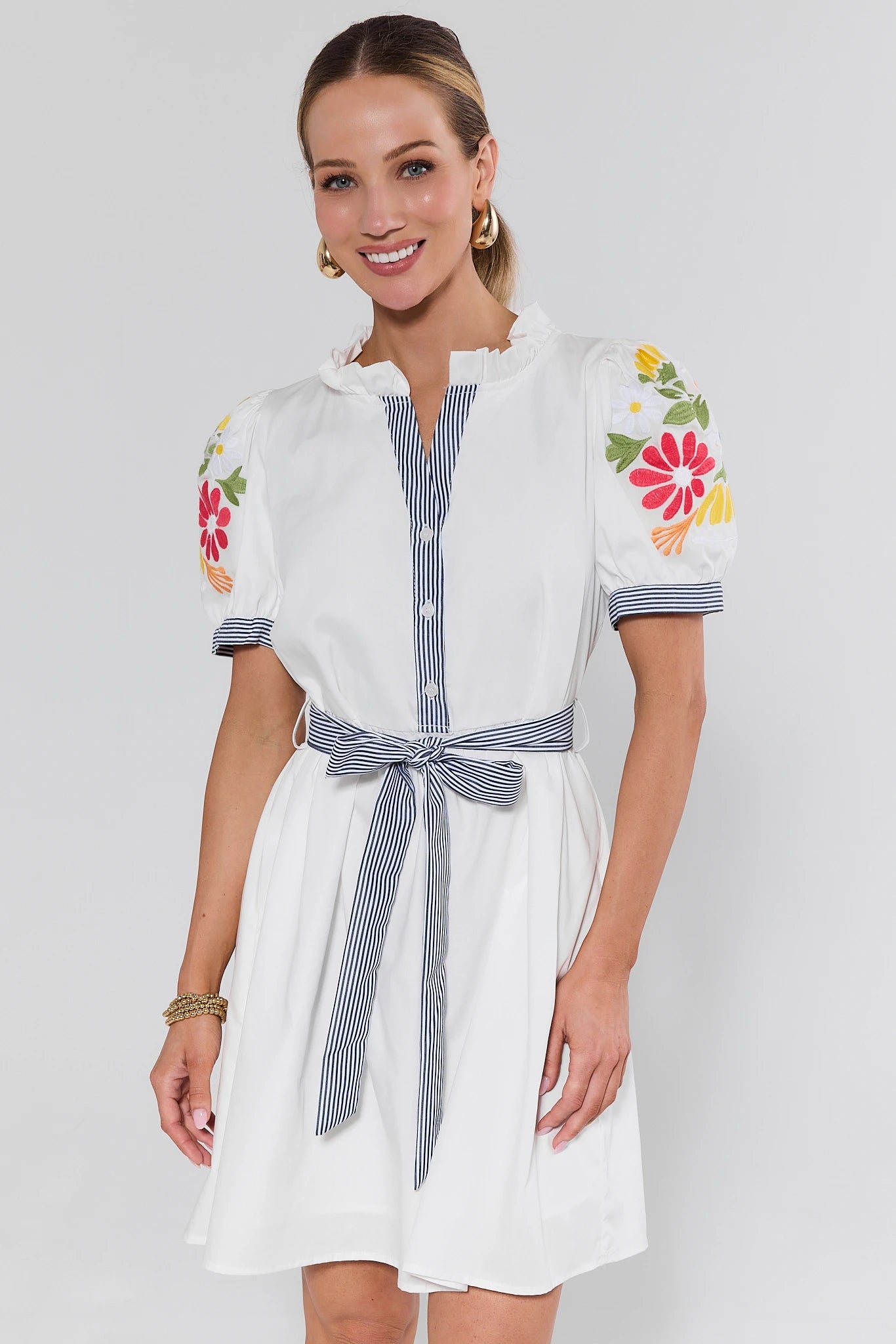 Woman wearing a white dress with floral embroidery on a plain background