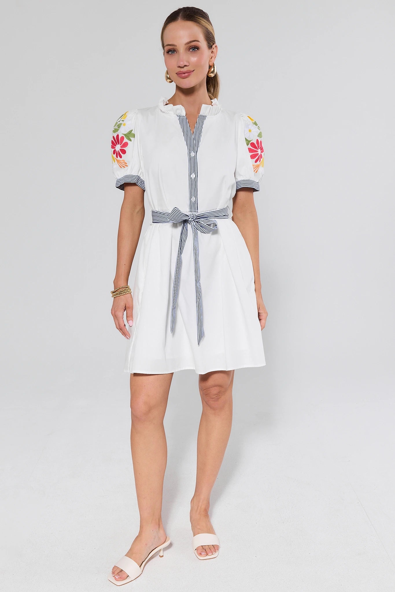 Woman wearing a white dress with floral embroidery on a plain background