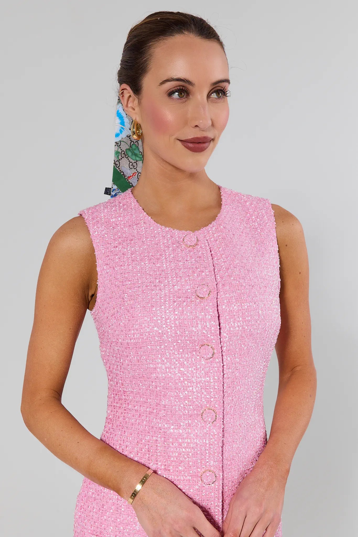 Woman wearing a pink sleeveless dress with buttons on a gray background