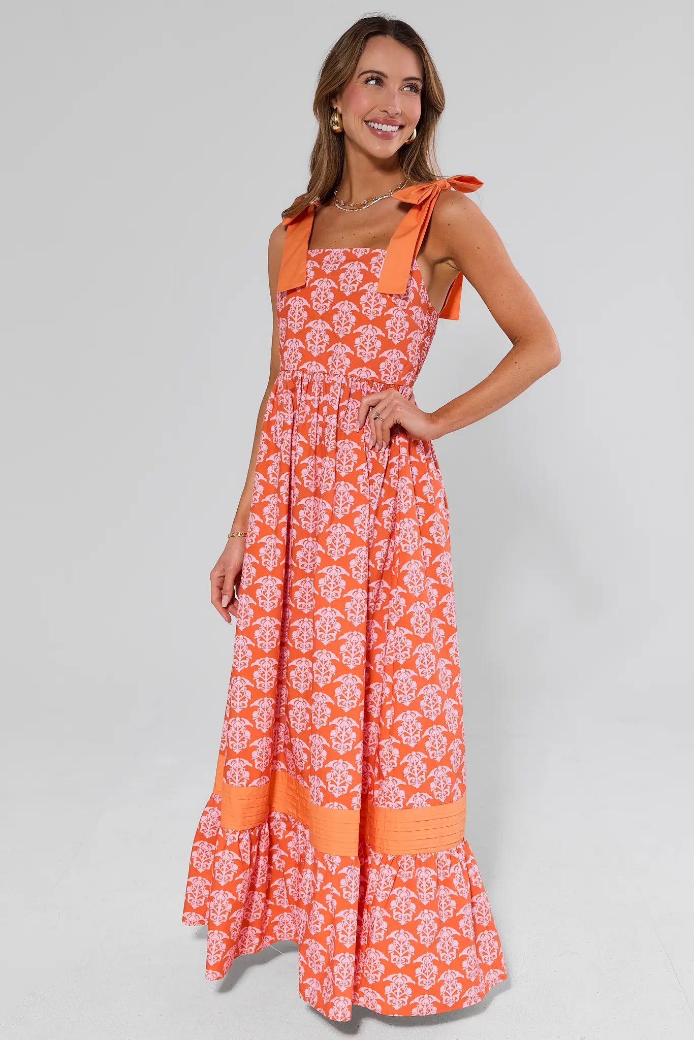 Woman wearing an orange floral maxi dress on a gray background