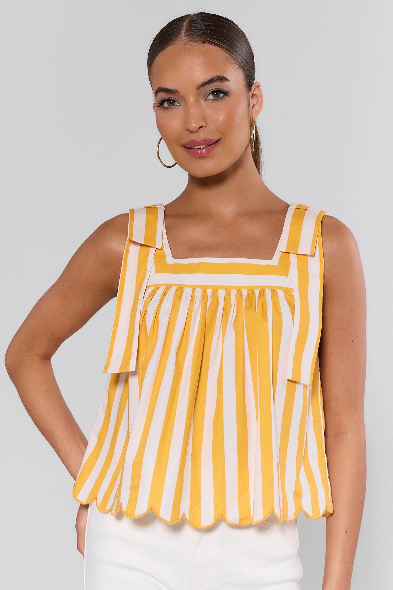 Woman wearing a yellow and white striped sleeveless top against a plain background