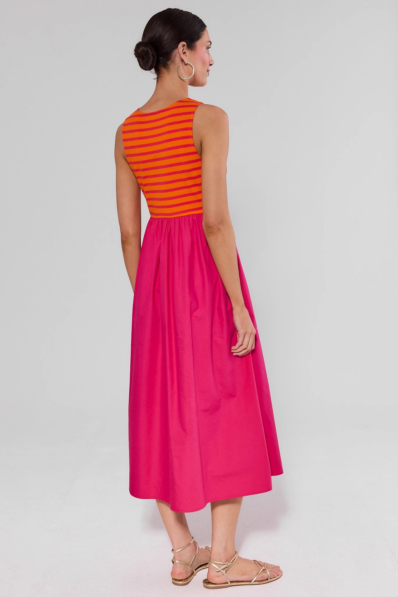 Woman standing wearing a pink dress with an orange striped top on a white background