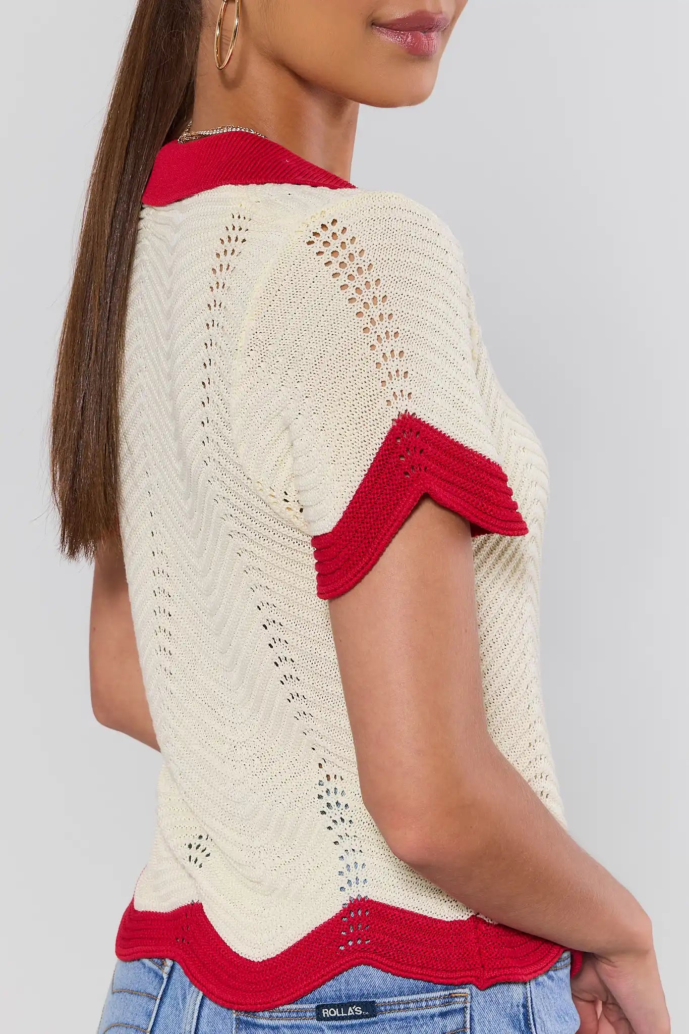 side shot Woman wearing a cream and red knitted top with a plain background