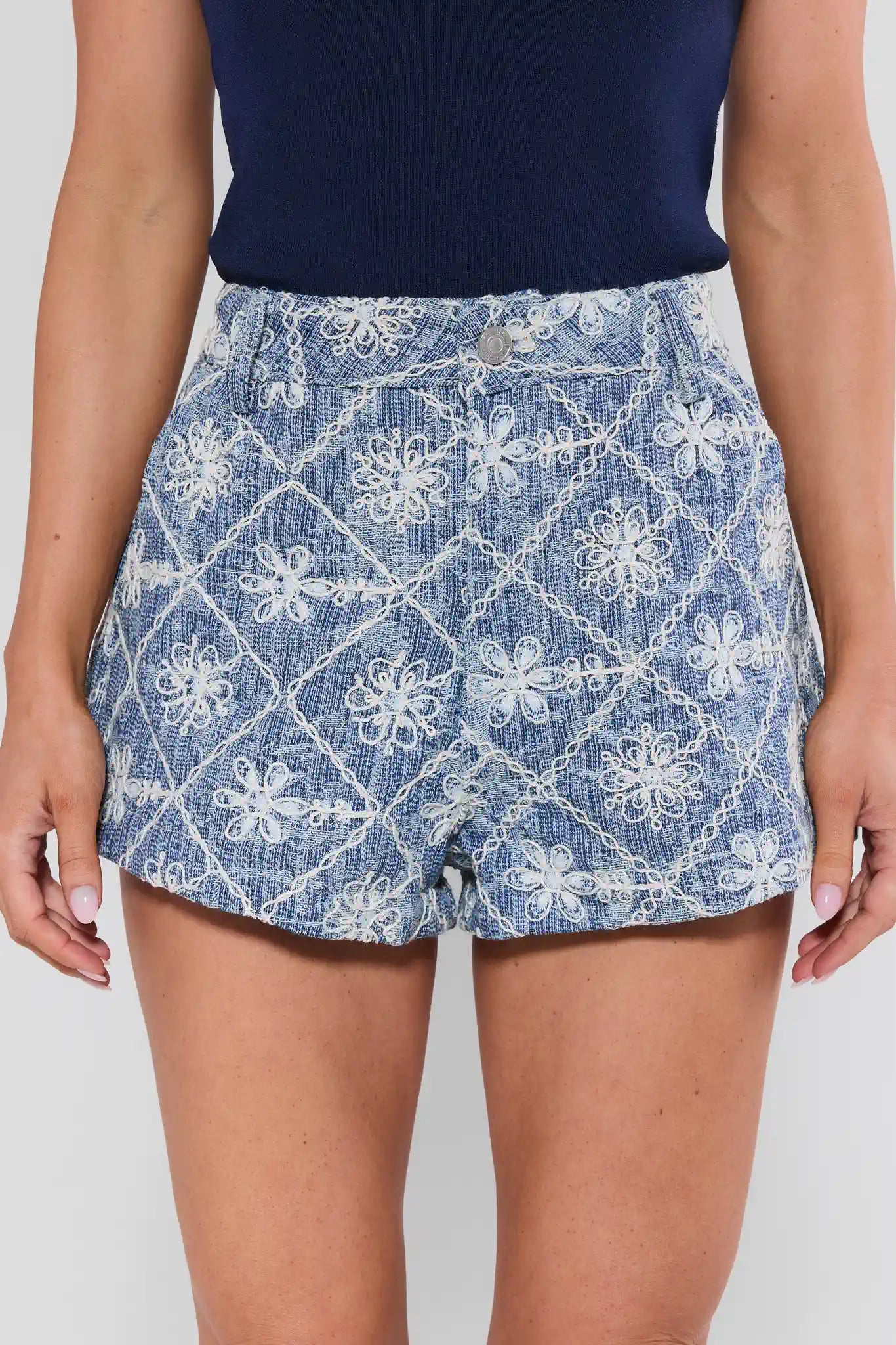 Person wearing a blue denim skirt with white floral patterns on a plain background