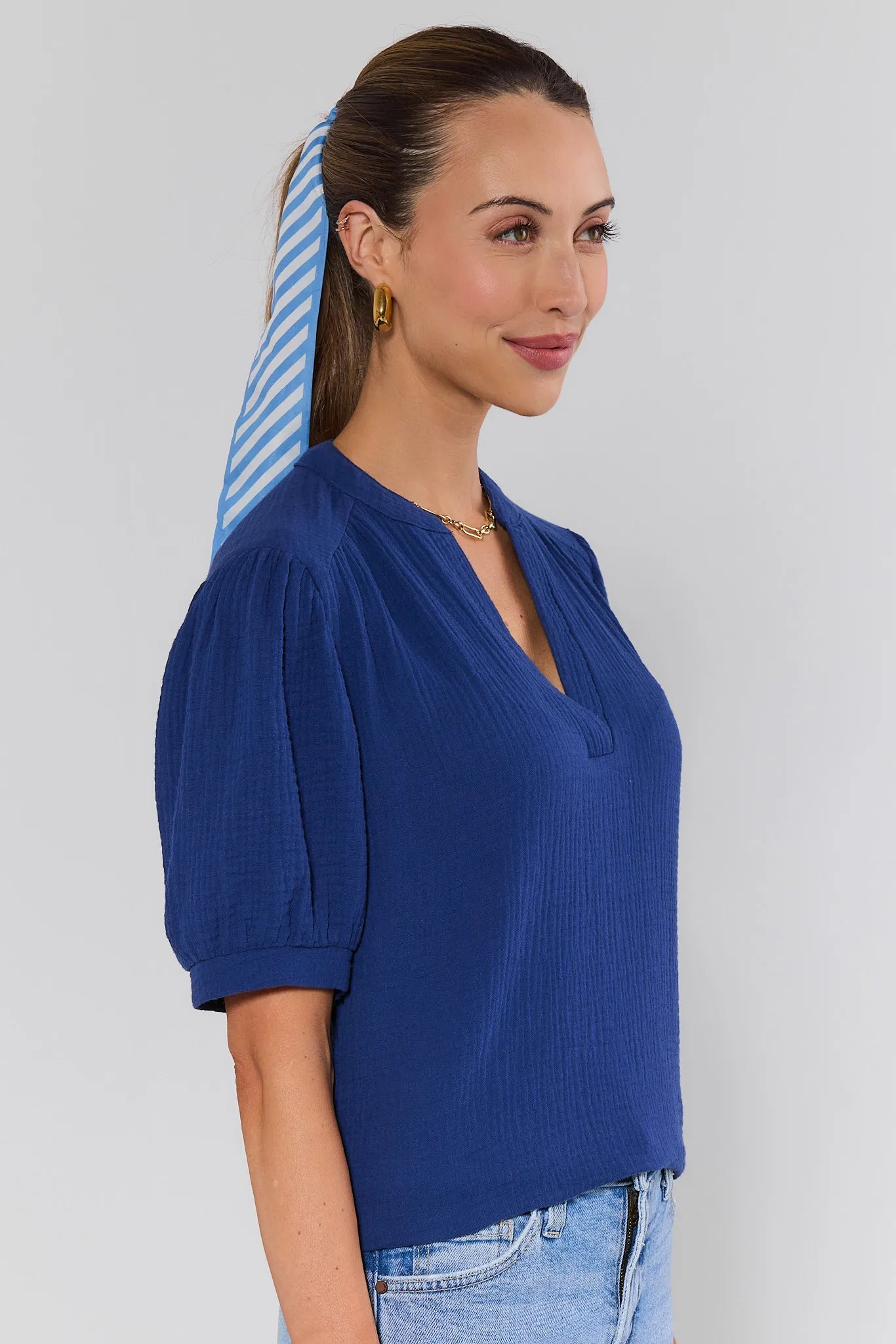 side shot Woman wearing a blue top with puffed sleeves against a plain background