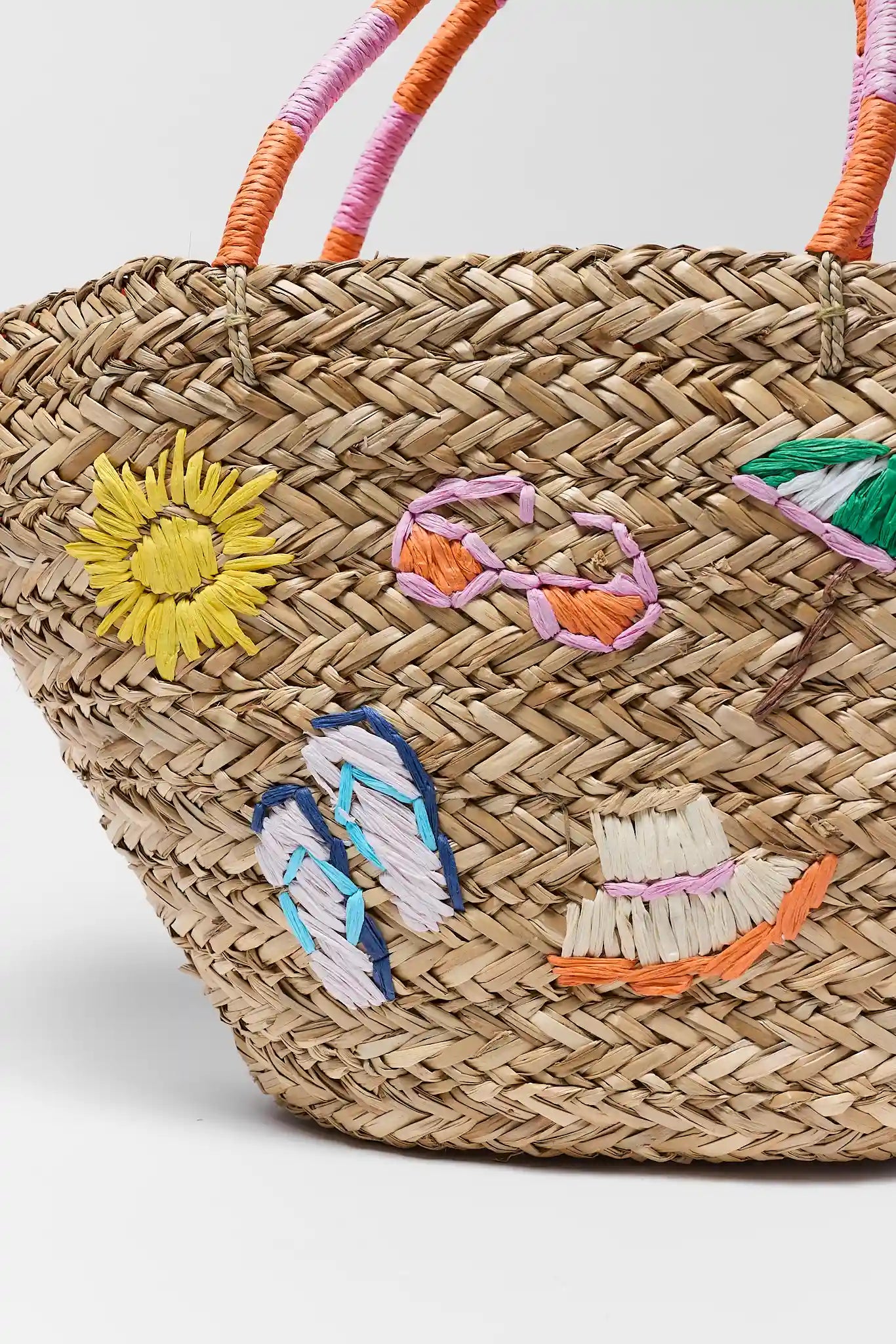 close up Woven straw bag with colorful embroidered designs on a light gray background